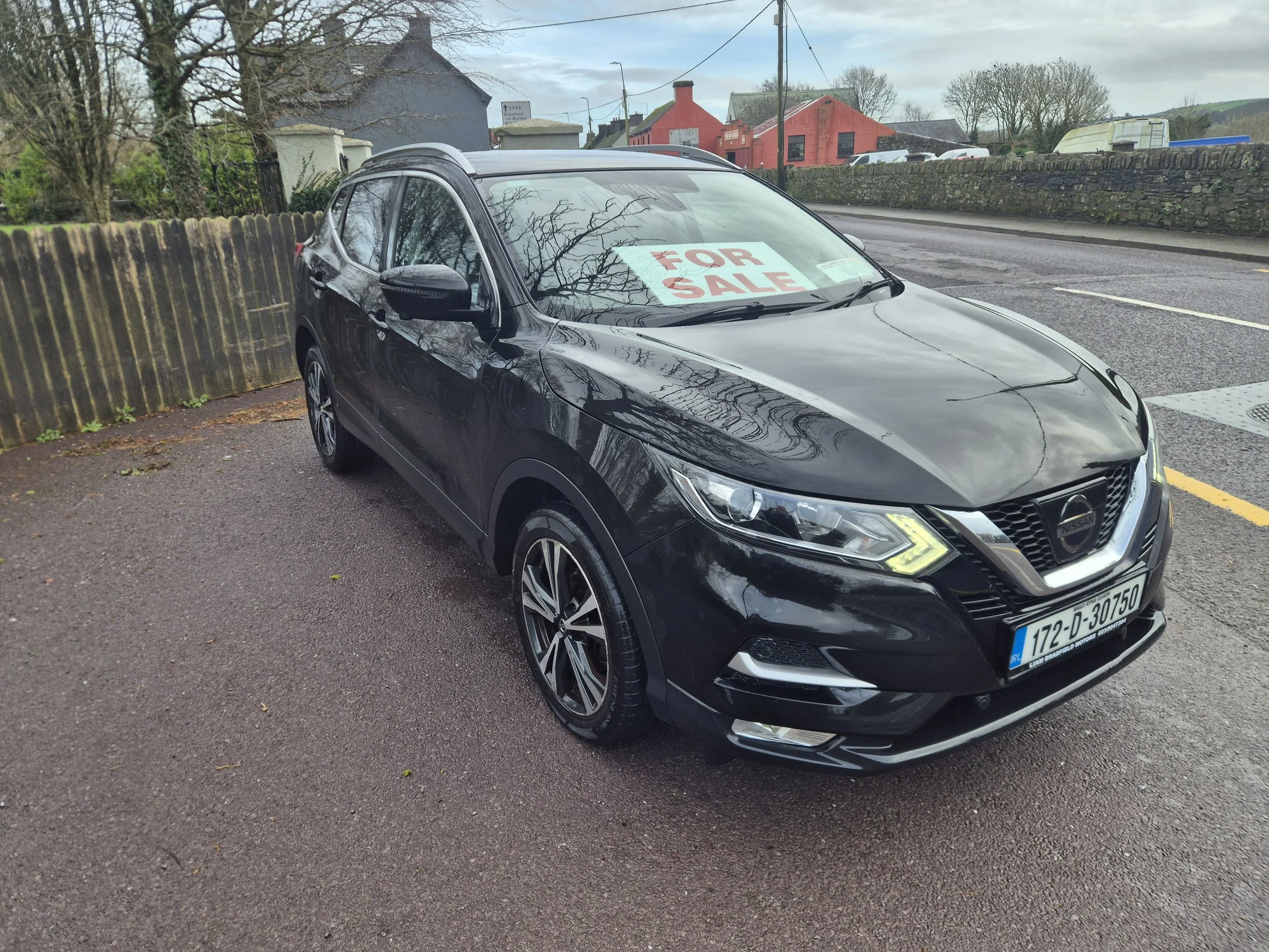 Black Nissan car parked on the side of the road with a 'For Sale' sign in the windshield.
