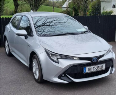 Silver Toyota hatchback car parked in a driveway with trees and a black fence in the background.