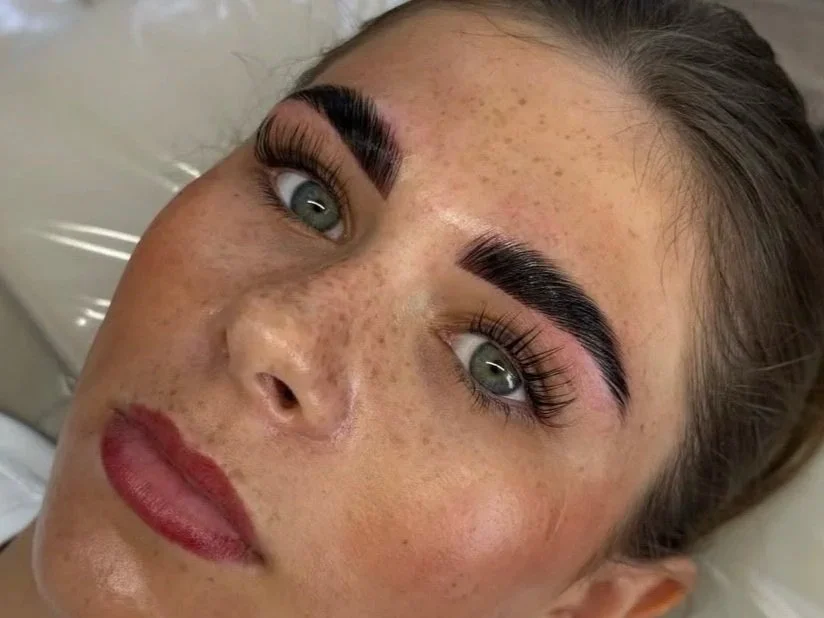 Close-up portrait of a woman with green eyes, freckles, defined eyebrows, long eyelashes, and pink lips