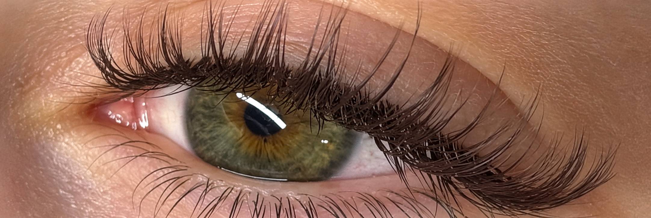 Extreme close-up of a green and hazel human eye with long dark eyelashes