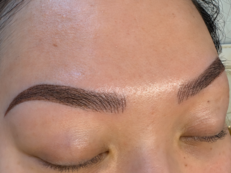 Close-up of a person's groomed, microbladed eyebrows with eyes closed