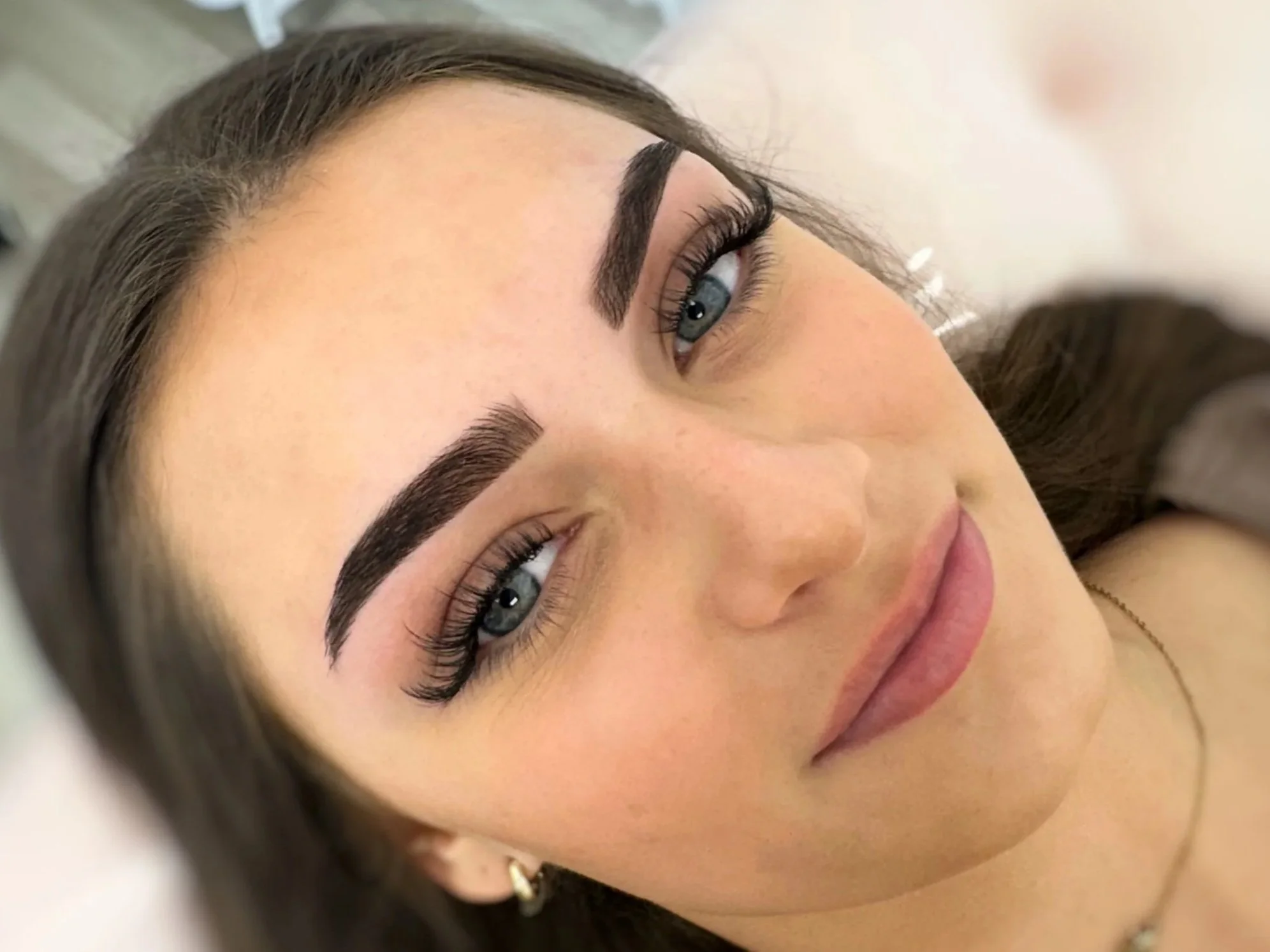 Close-up portrait of a woman with blue eyes, dark hair, defined eyebrows, and long eyelashes
