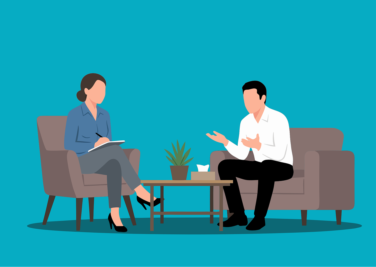 Illustration of a woman taking notes and a man talking in a therapy session or interview in a living room with a blue wall, sofa, armchair, potted plant, and coffee table in between.