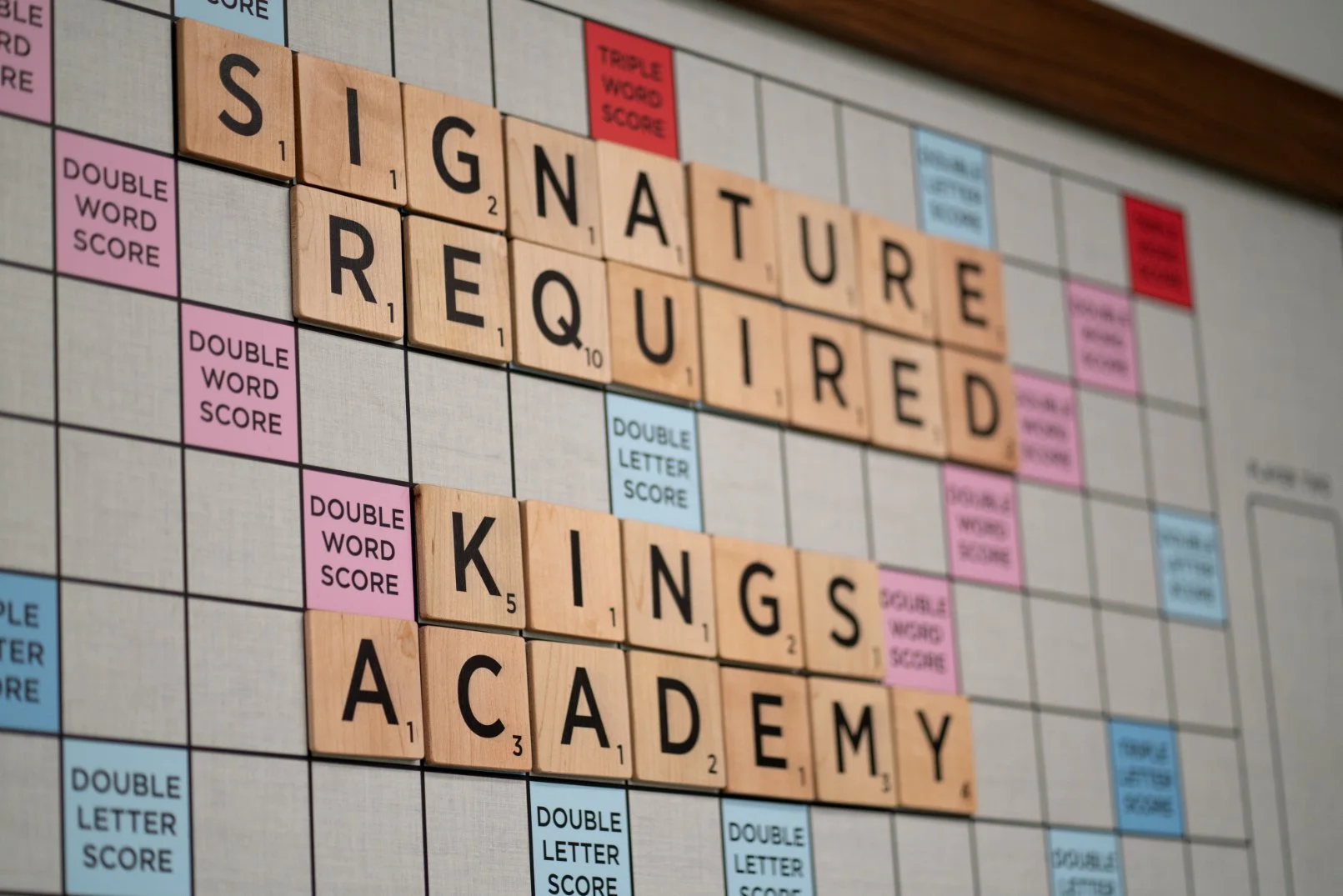 Scrabble board with words 'Signature Required' and 'Kings Academy' spelled out with letter tiles.