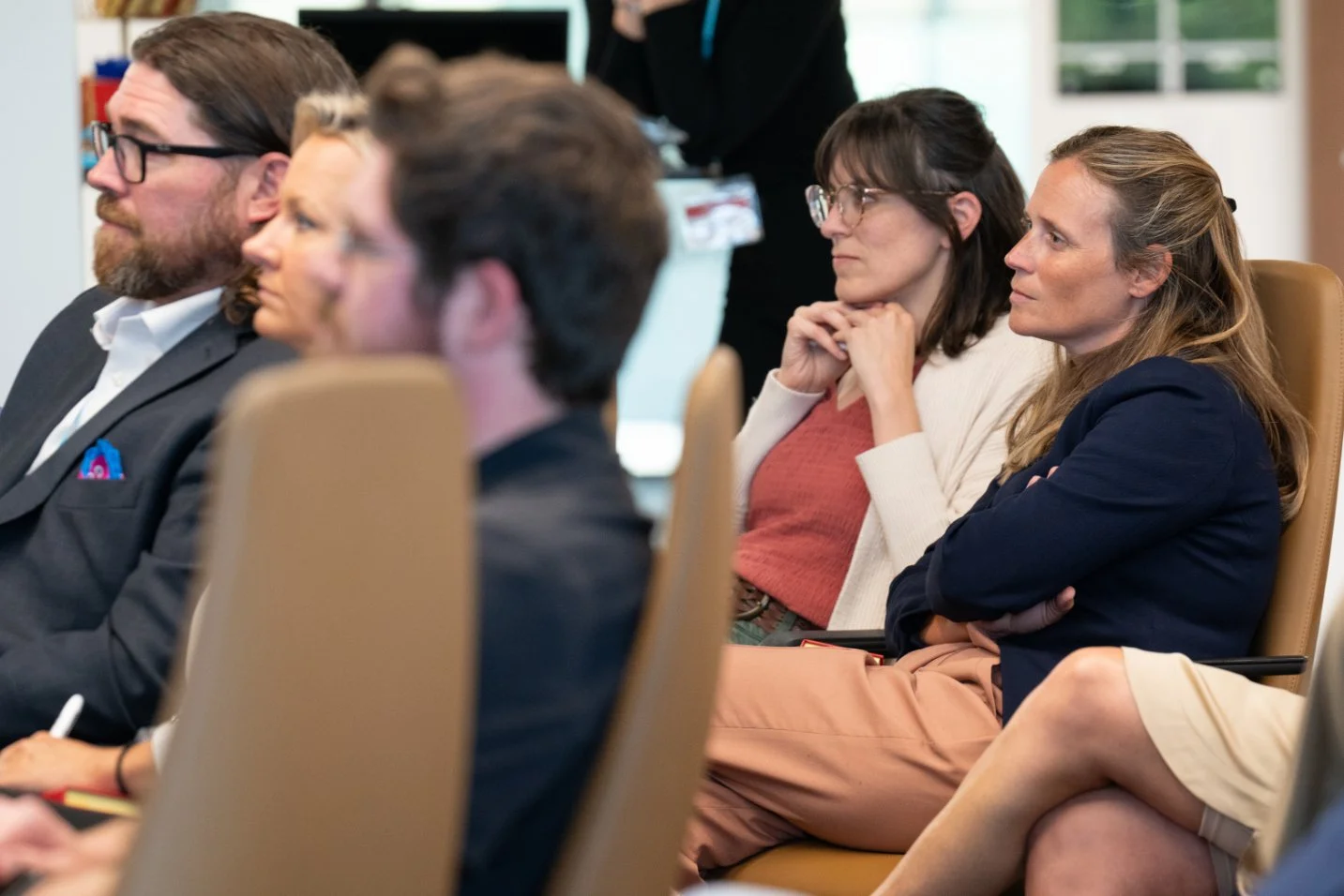 People attending a conference or seminar, seated in a row, listening attentively.