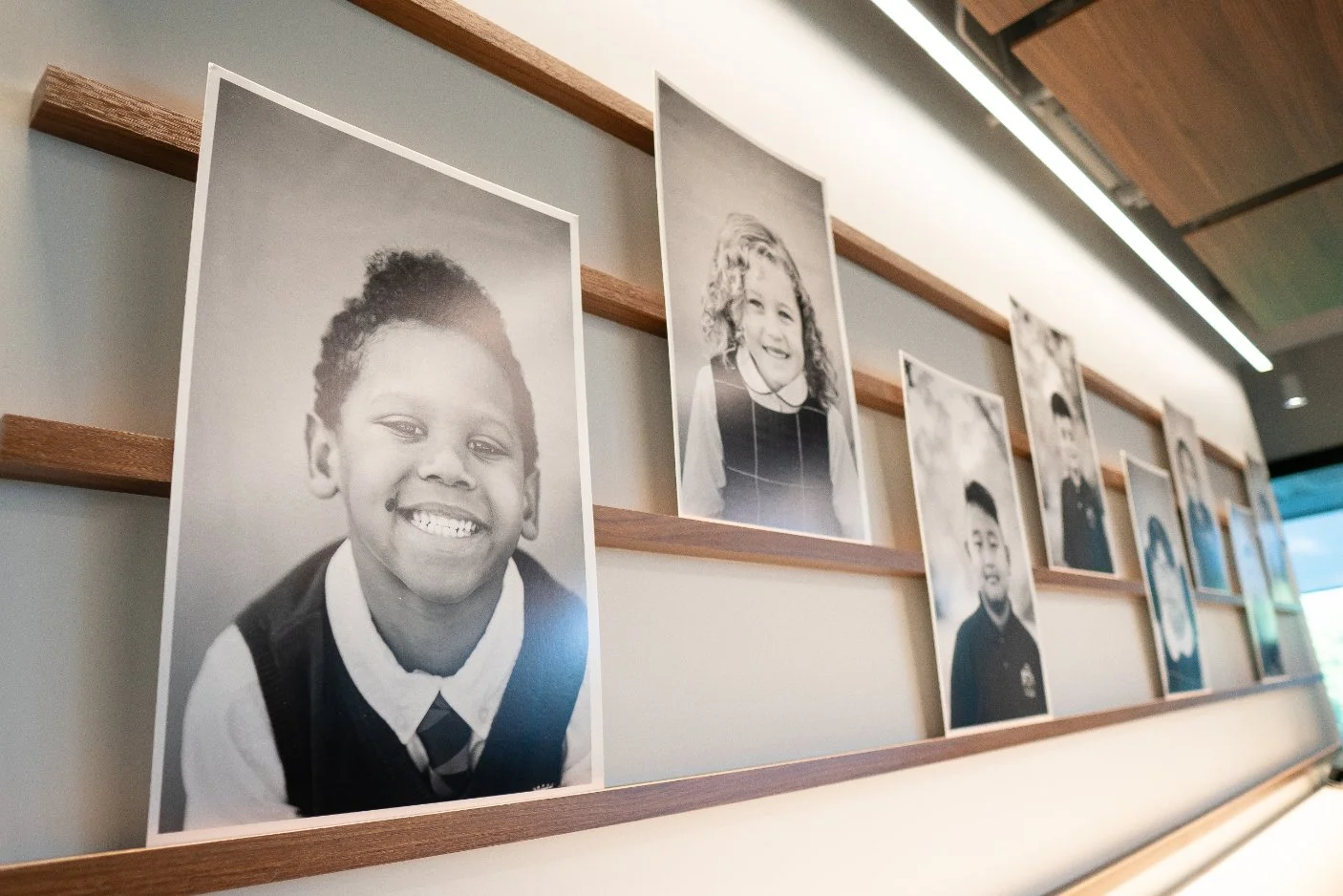 Black and white photographs of children displayed on wooden shelves on a wall, with some children smiling and others with neutral expressions.
