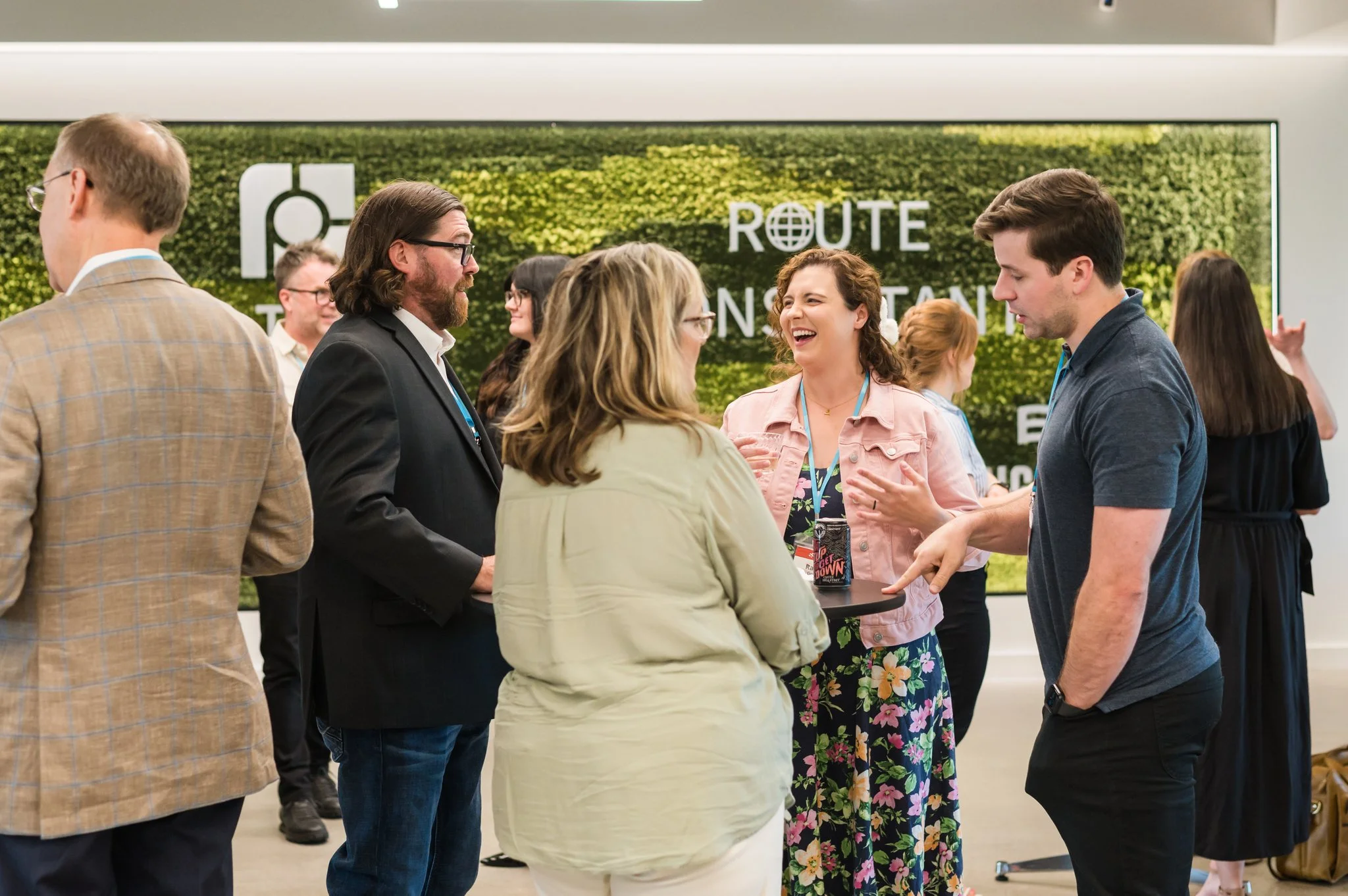 People engaged in conversation at a networking event in a modern space with a green wall and signage in the background.