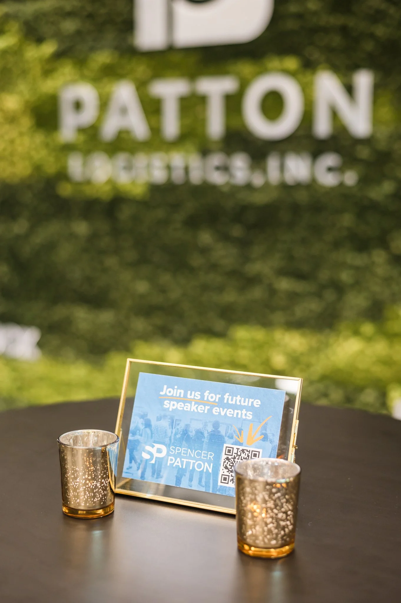 Sign on table promoting future speaker events featuring Spencer Patton, with two metallic candle holders.