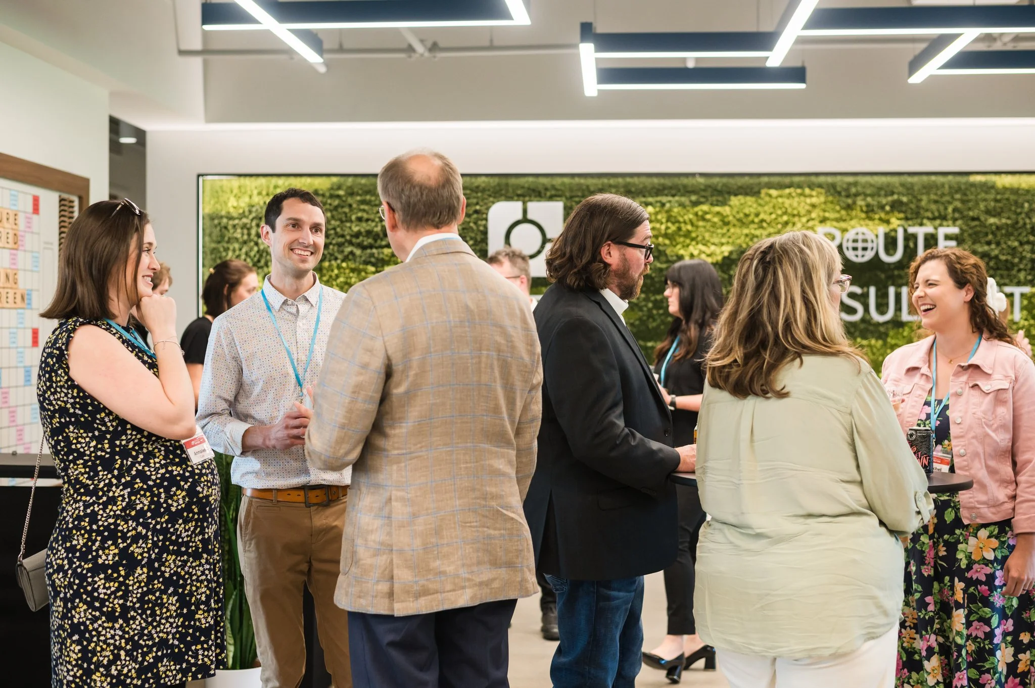 People gathered and talking at a networking event or conference, standing indoors with bright lighting and a green wall in the background.