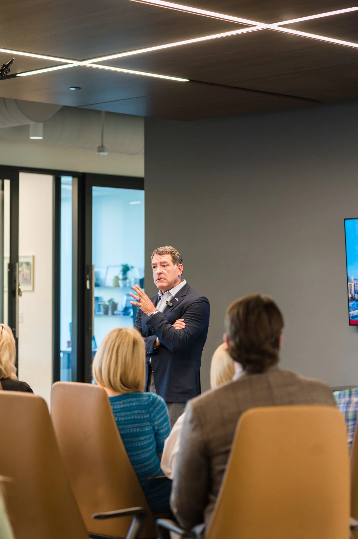 A man in a suit giving a speech to an audience seated in a conference room.