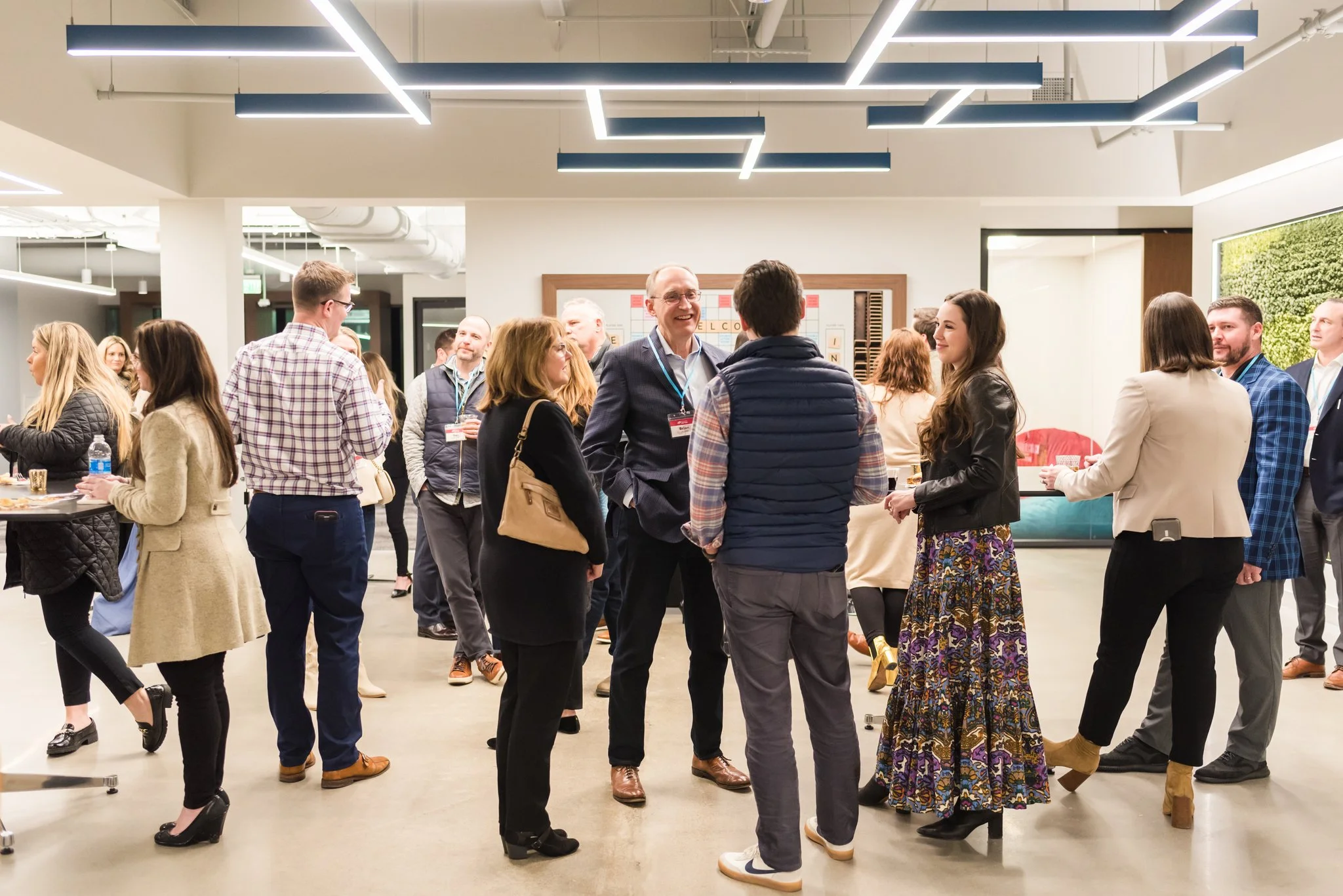 Group of people at a professional networking event or conference, engaging in conversations inside a modern, well-lit room.