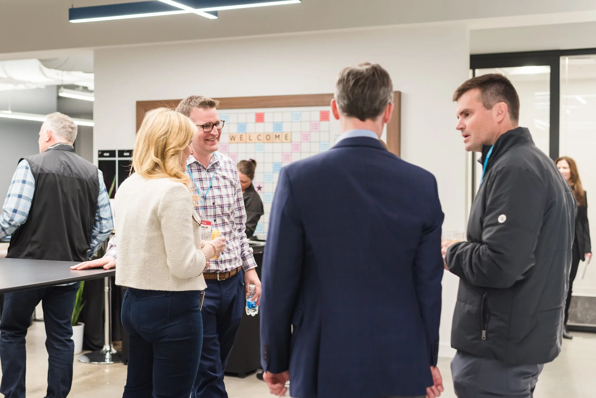Group of people talking at a professional networking event or conference in an indoor setting with a welcome board in the background.