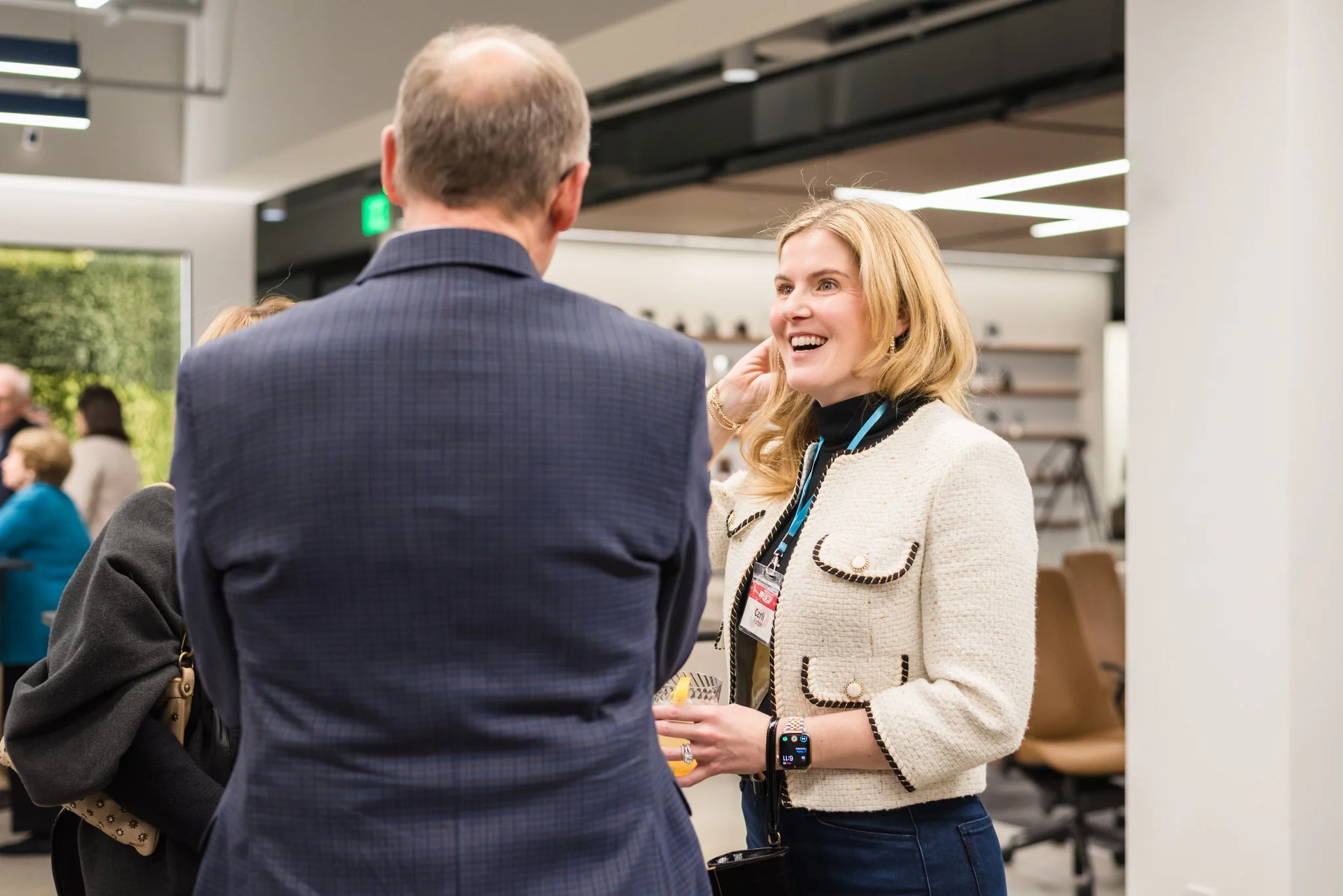 A woman with blonde hair smiling and talking to a man with light brown hair in a suit at a networking event or conference.