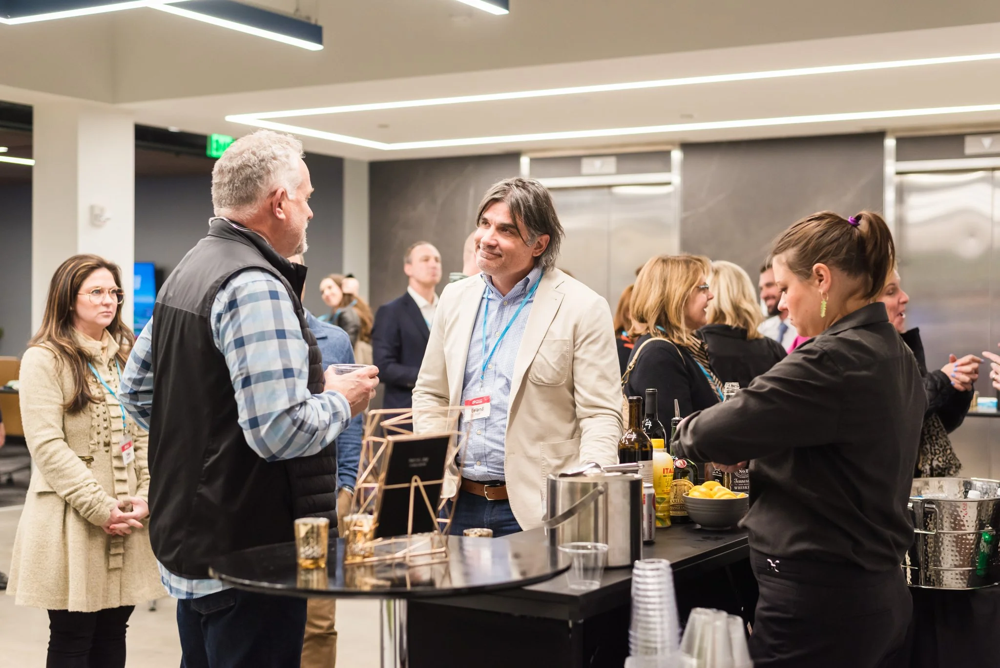 People socializing at a networking event in a modern indoor venue with a bar area, bottles, lemons, and glasses on the counter.