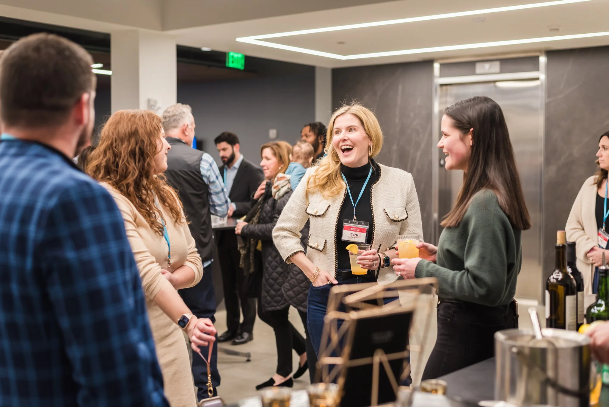 People socializing at a professional networking event with drinks in hand, engaging in conversation in a modern indoor setting.