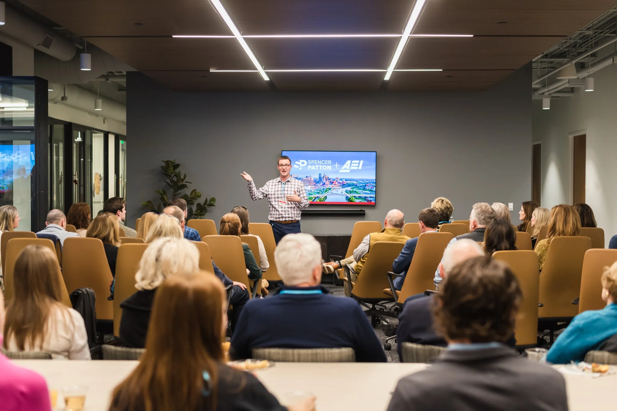 A man giving a presentation to a group of people in a conference room, with a screen displaying 'Spencer Patton + AEI' behind him.