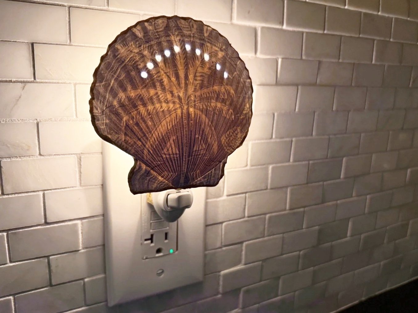 An electrical wall outlet with a lampshade made from a dried palm leaf placed over the bulb, creating a decorative light fixture against a white brick wall.