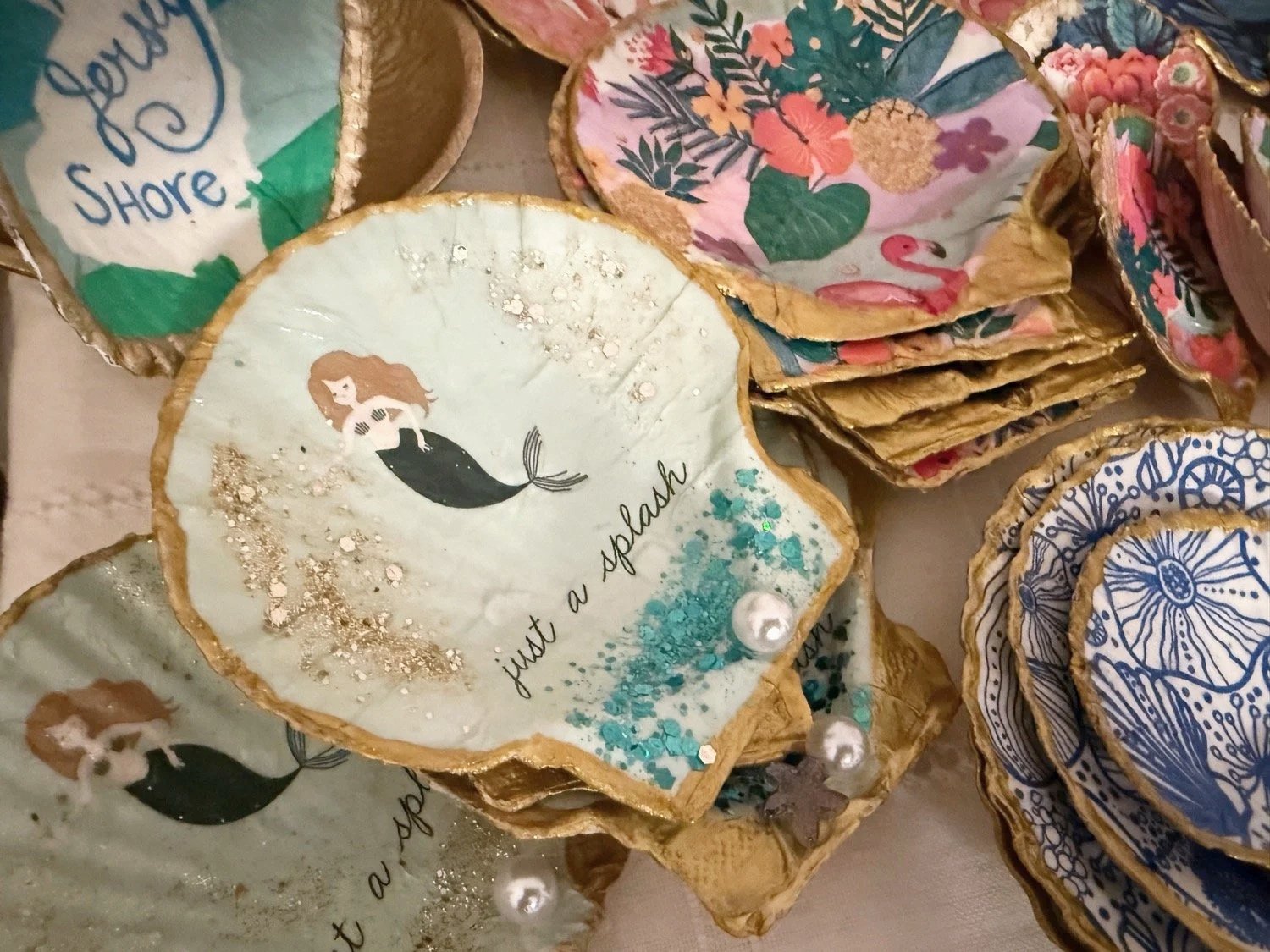 Decorative coasters with various colorful patterns and illustrations, including a mermaid with the phrase 'just a splash' and seashells, on a table.