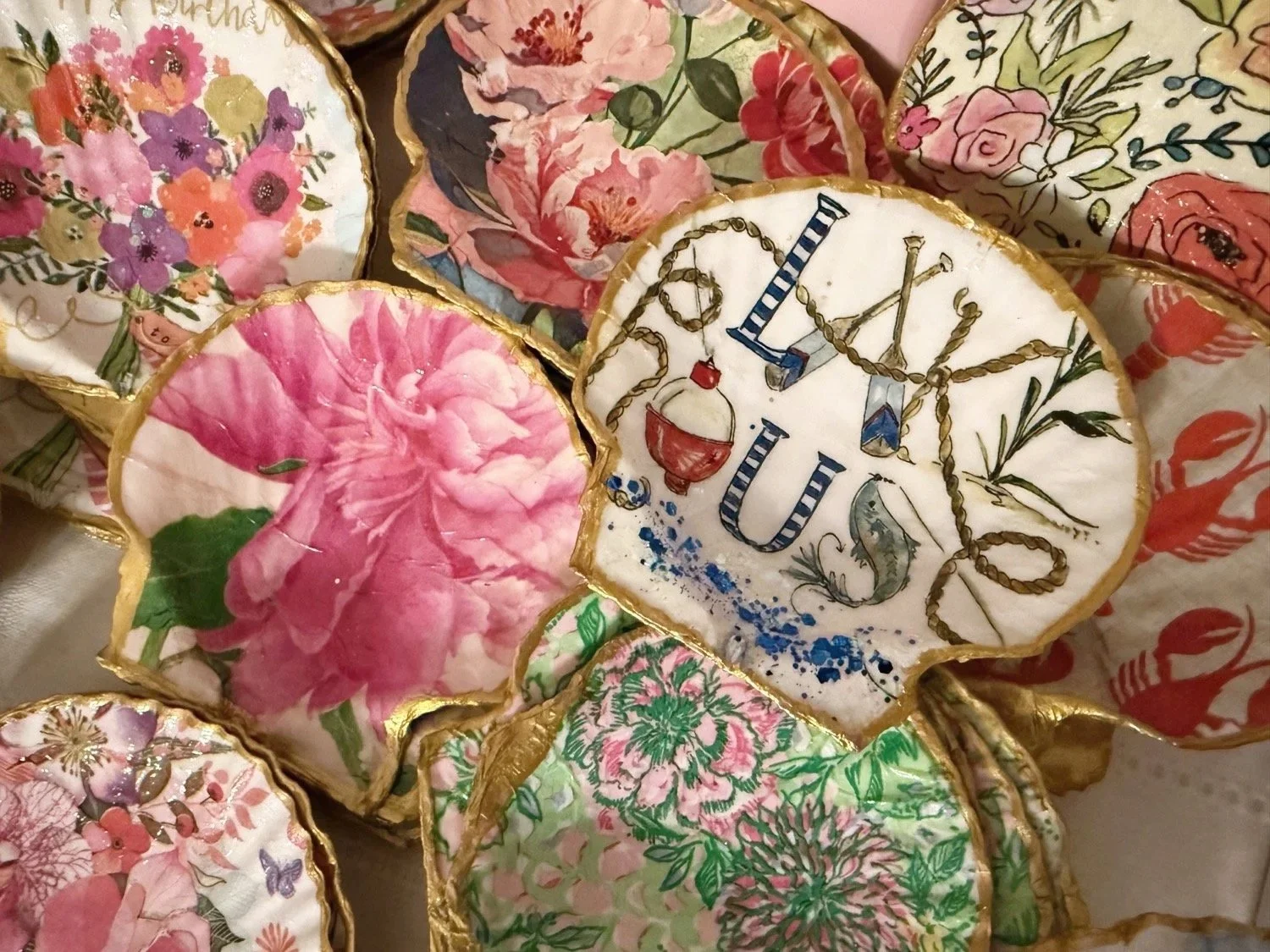 Decorative ceramic plates with floral patterns and the word "LOVE" painted on one, arranged together. Plates have gold trim and feature various colorful flower designs.