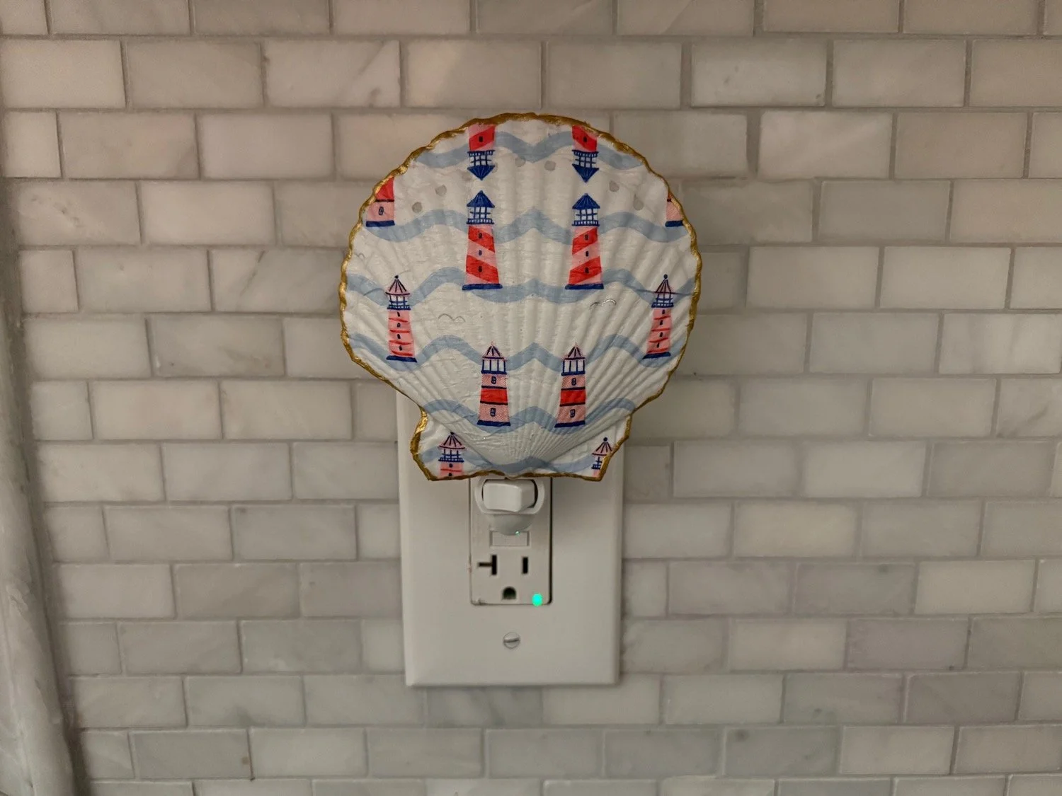 A paper lantern with lighthouse illustrations, hanging over a power outlet on a brick wall.