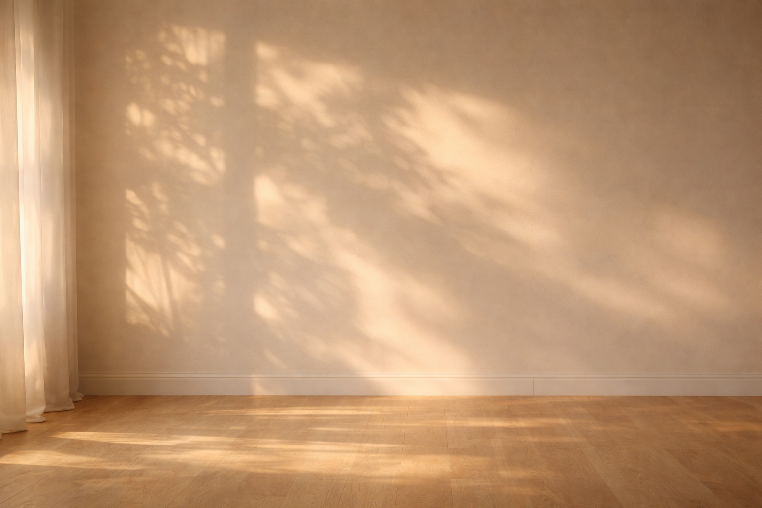 Empty room with sunlight casting shadows on the beige wall and hardwood floor, and a white curtain partially visible on the left side.
