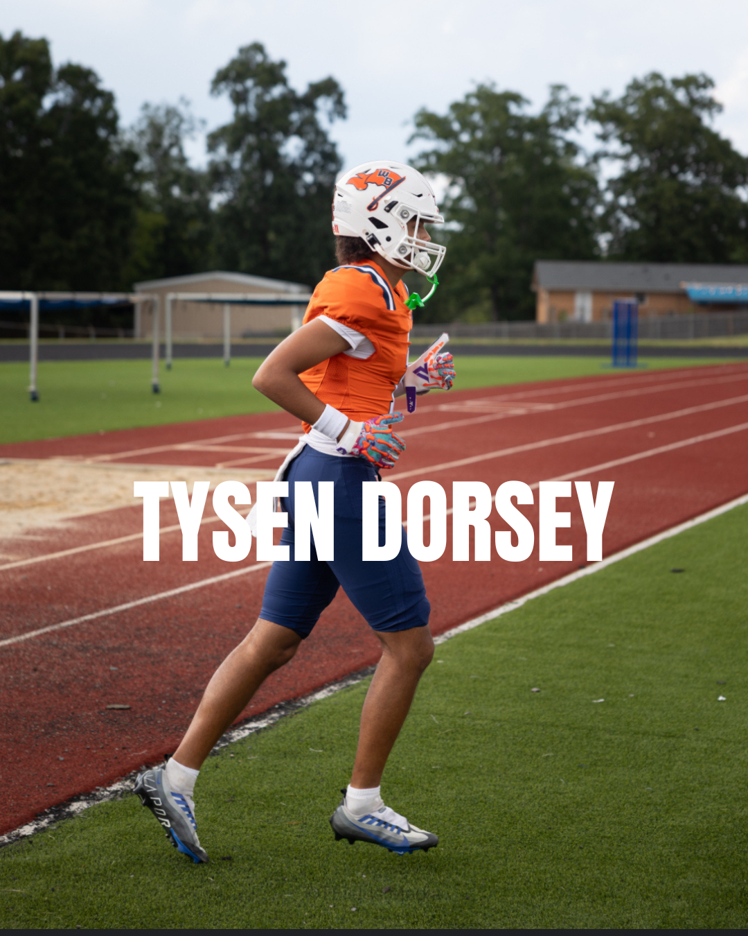 A football player in orange and blue uniform running on a track at a sports field, wearing a helmet and gloves.