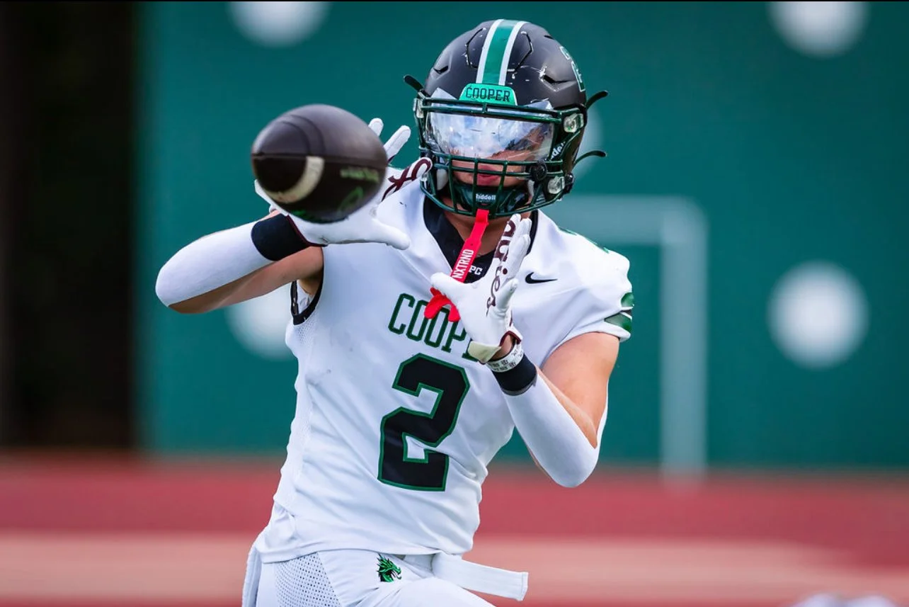 An American football player wearing a white jersey with the number 2 and the word 'Coppell' in green, holding a football in a throwing stance, with a black helmet, facing forward on a football field.