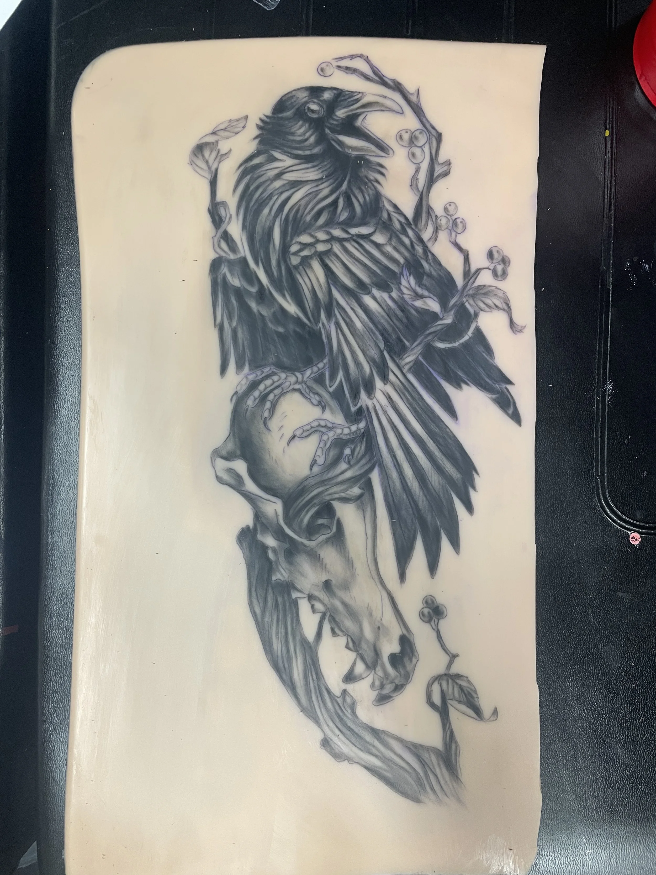 Black and white tattoo sketch of a raven perched on a branch with berries and leaves.