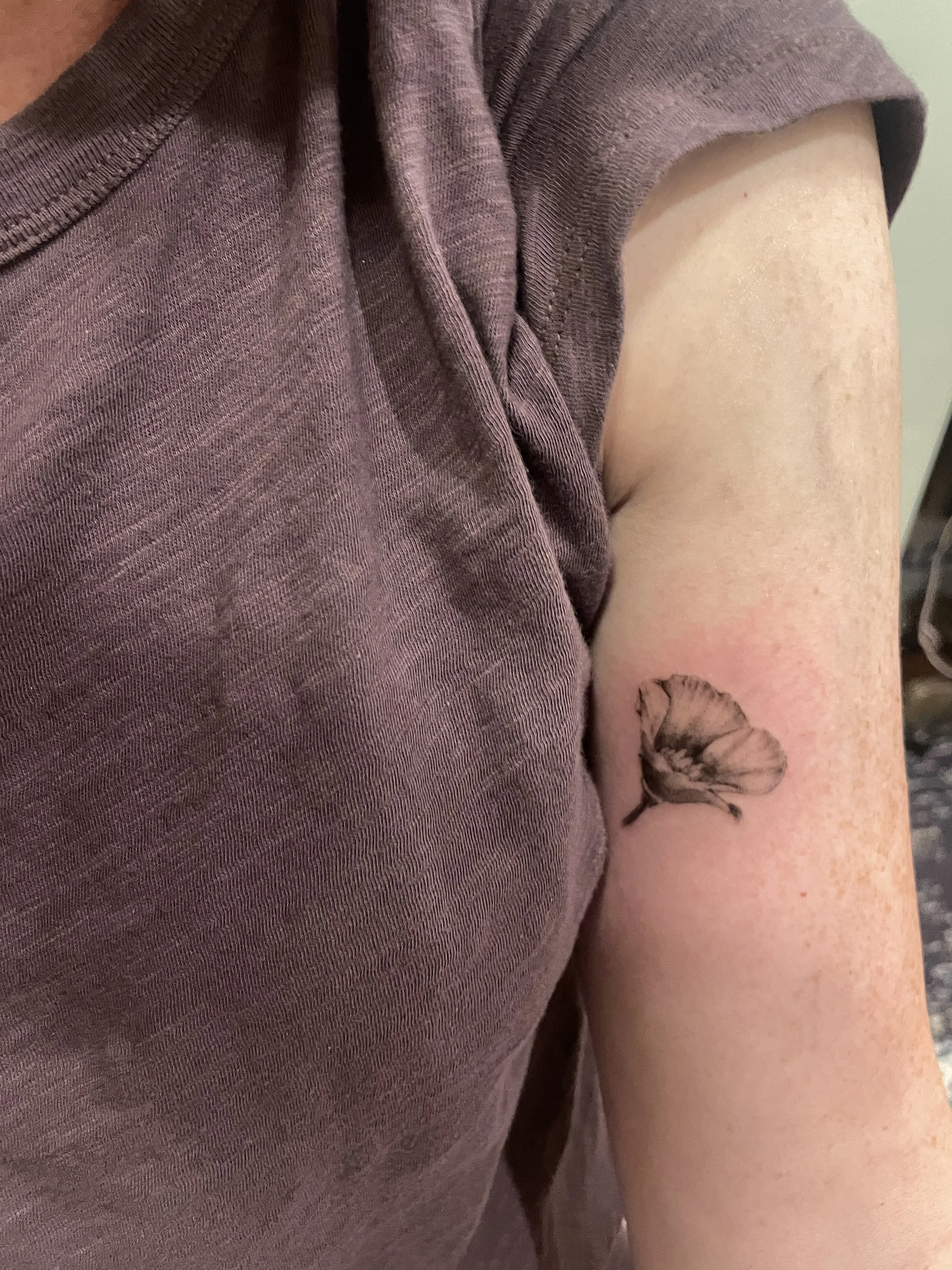 Close-up of a person's shoulder and upper arm with a tattoo of a flower.