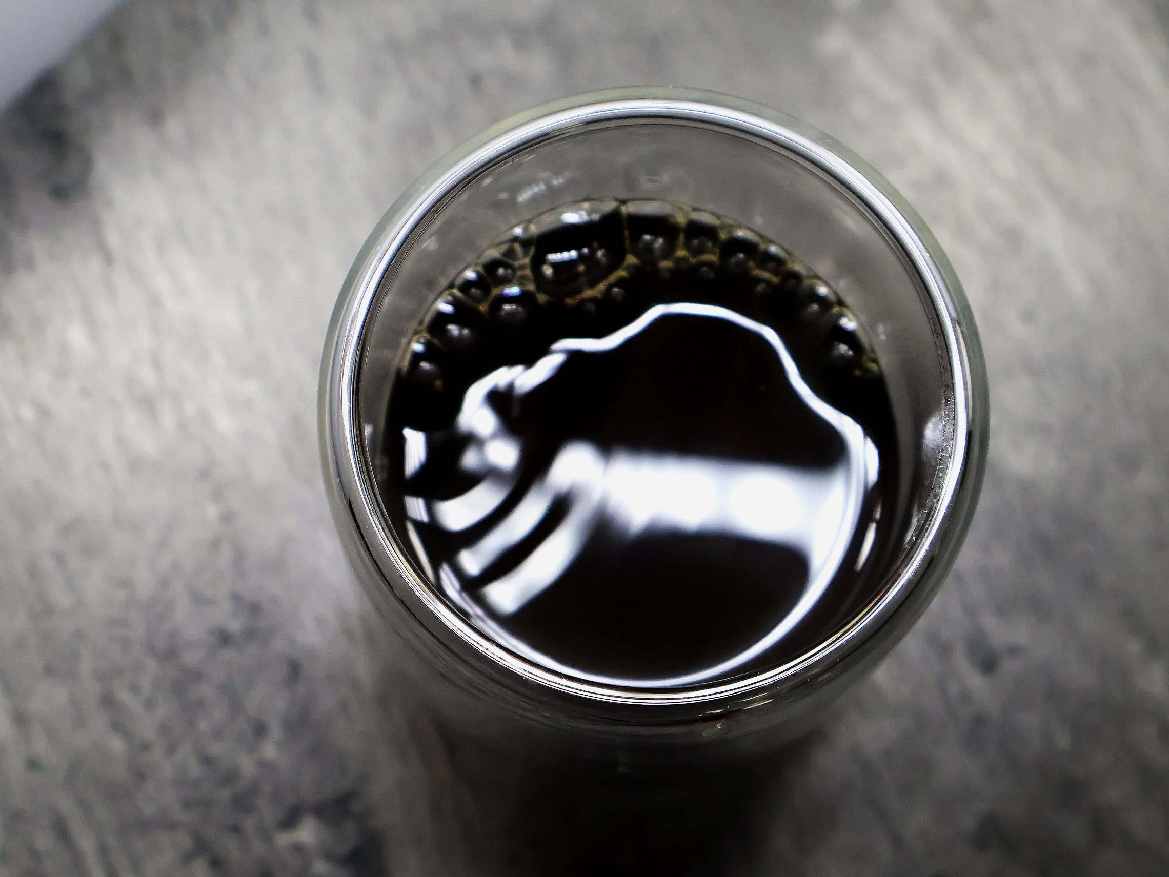 Vista superior de un vaso transparente con refresco oscuro y burbujas, colocación en una superficie grisácea.