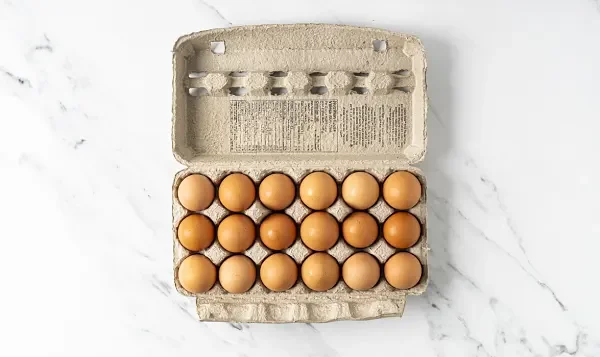 Open carton of brown eggs on a white marble surface.