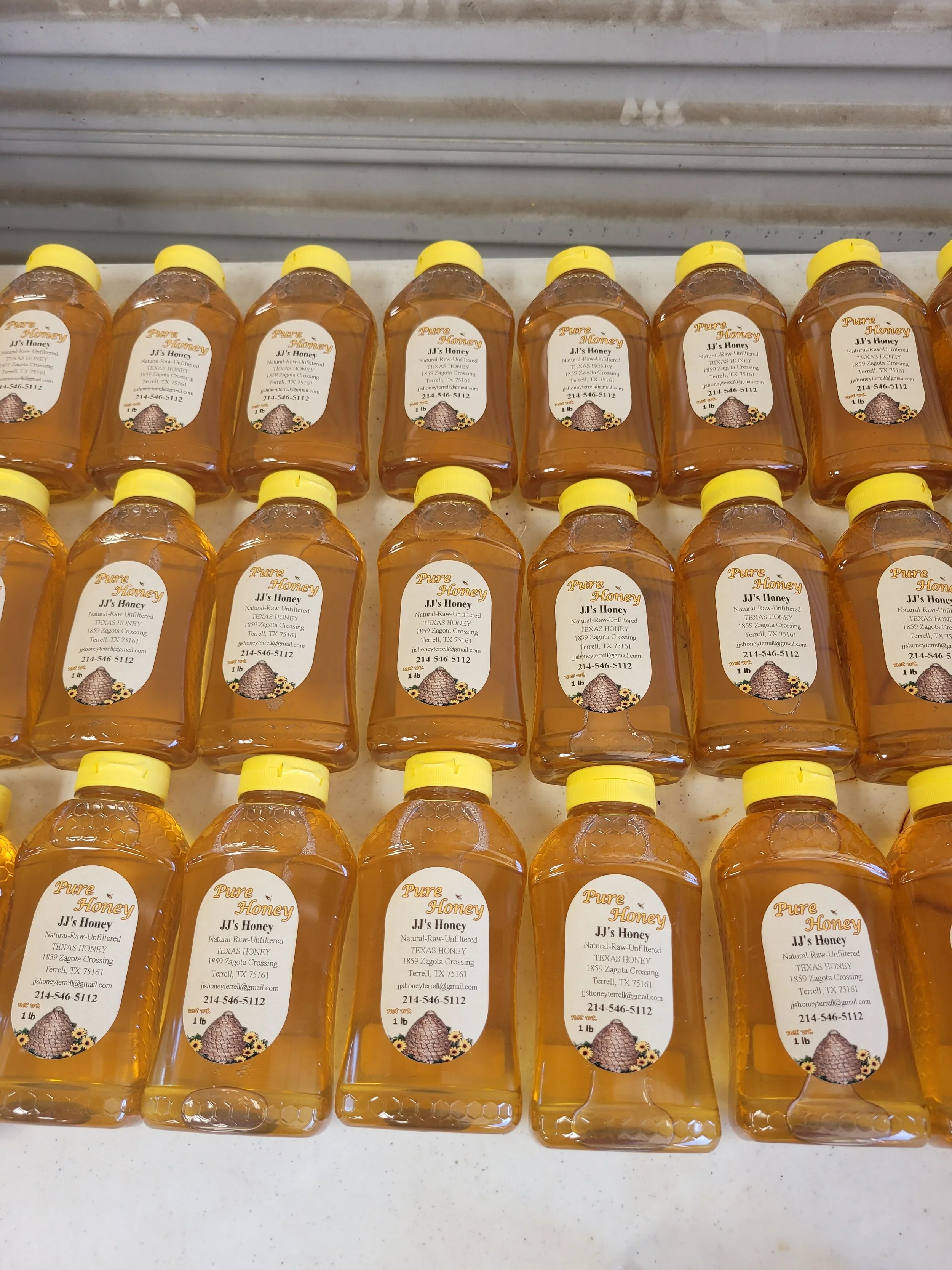 Multiple bottles of honey with yellow caps and white labels on a white surface.