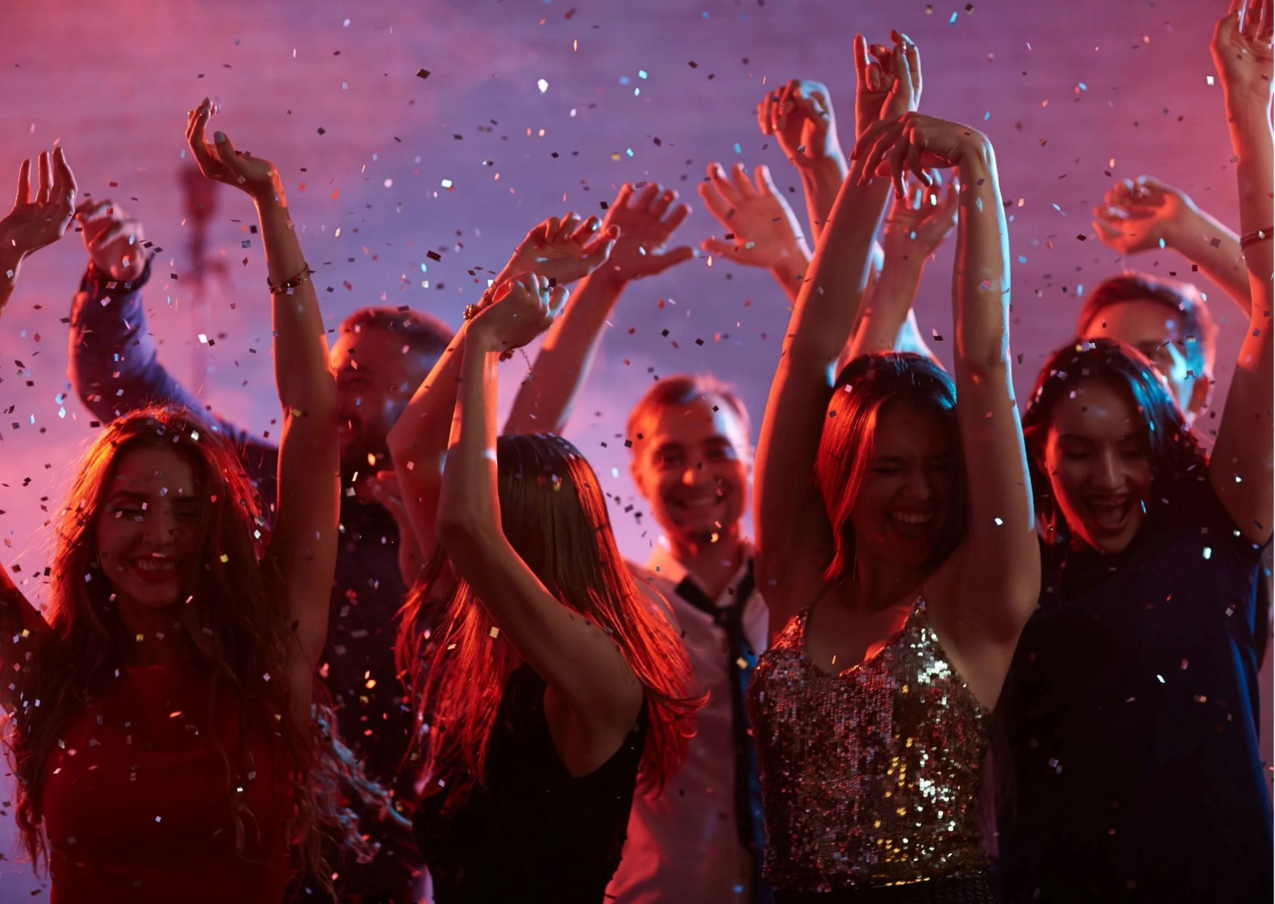 People celebrating at a party with confetti and colorful lighting, dancing and smiling.