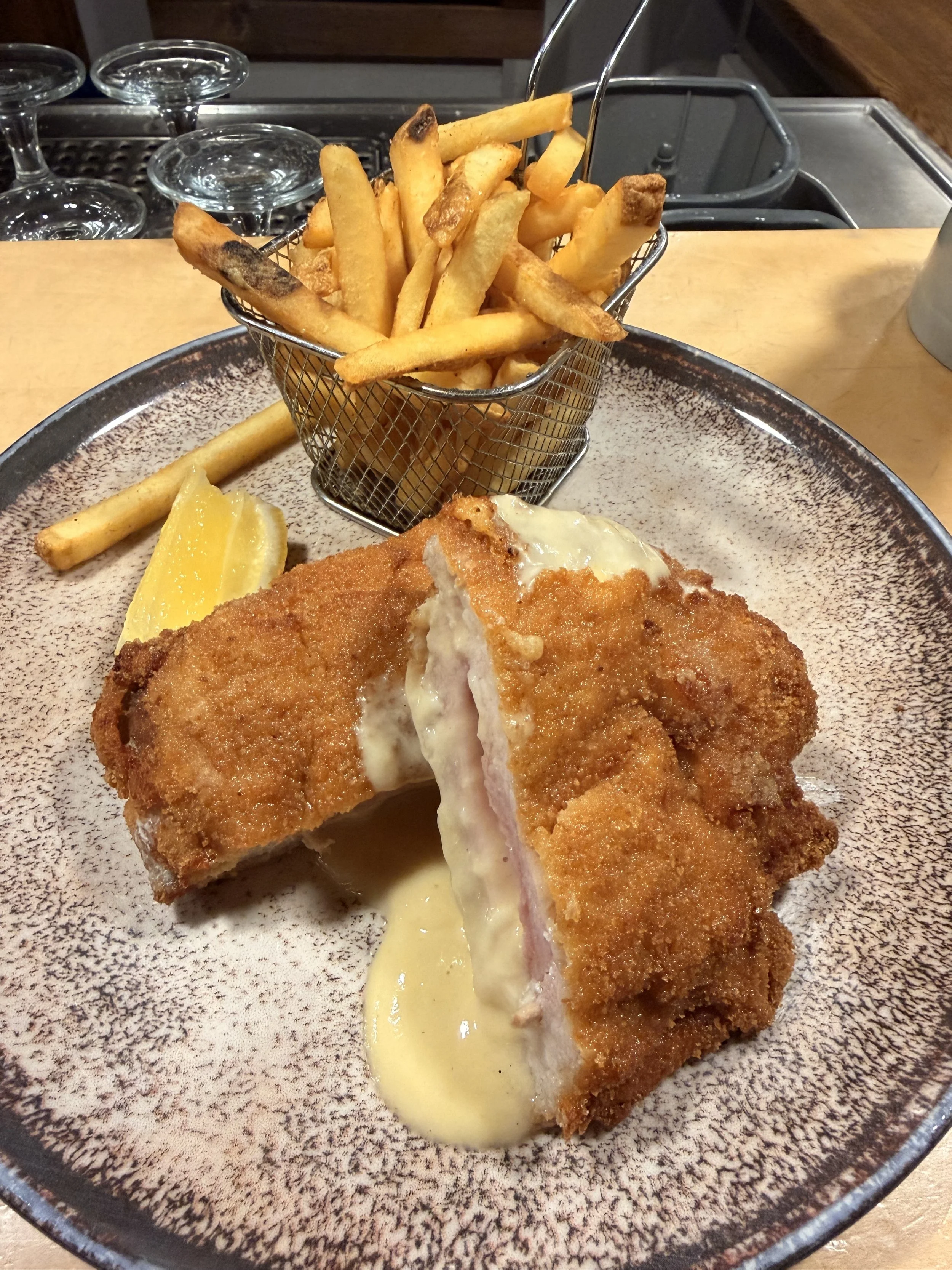 Panierte Fischfilets mit Zitronenscheiben und einer Sauce auf einem Teller, gekrönte Pommes frites in einem kleinen Metallkorb