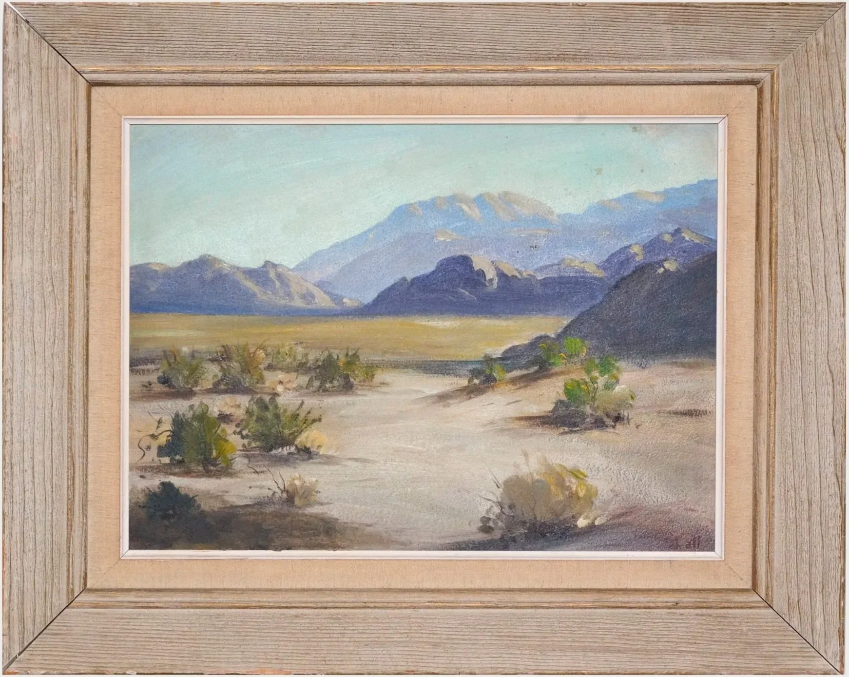 A framed watercolor painting of a desert landscape with mountains in the background, sparse vegetation, and a clear sky.