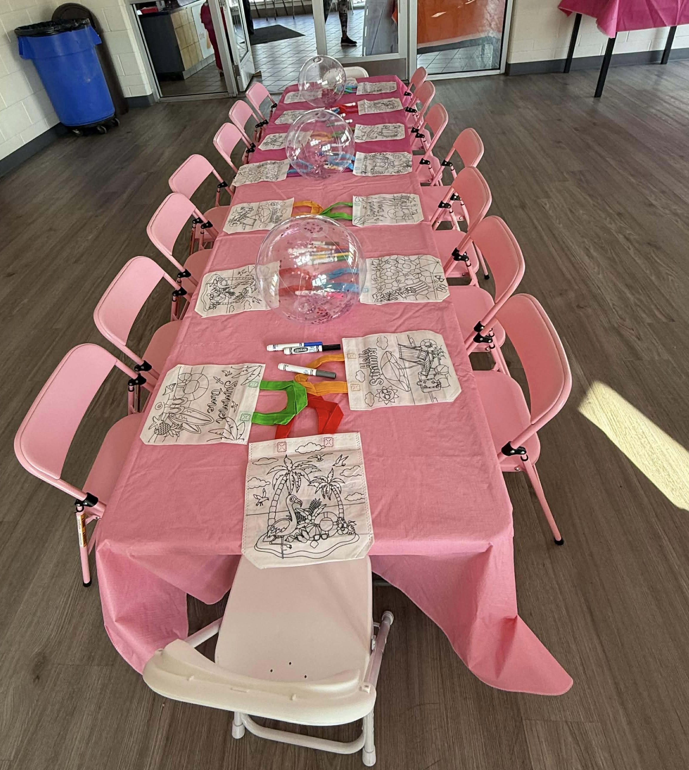 Pink kid sized chairs at a pink covered kid sized table with coloring pages