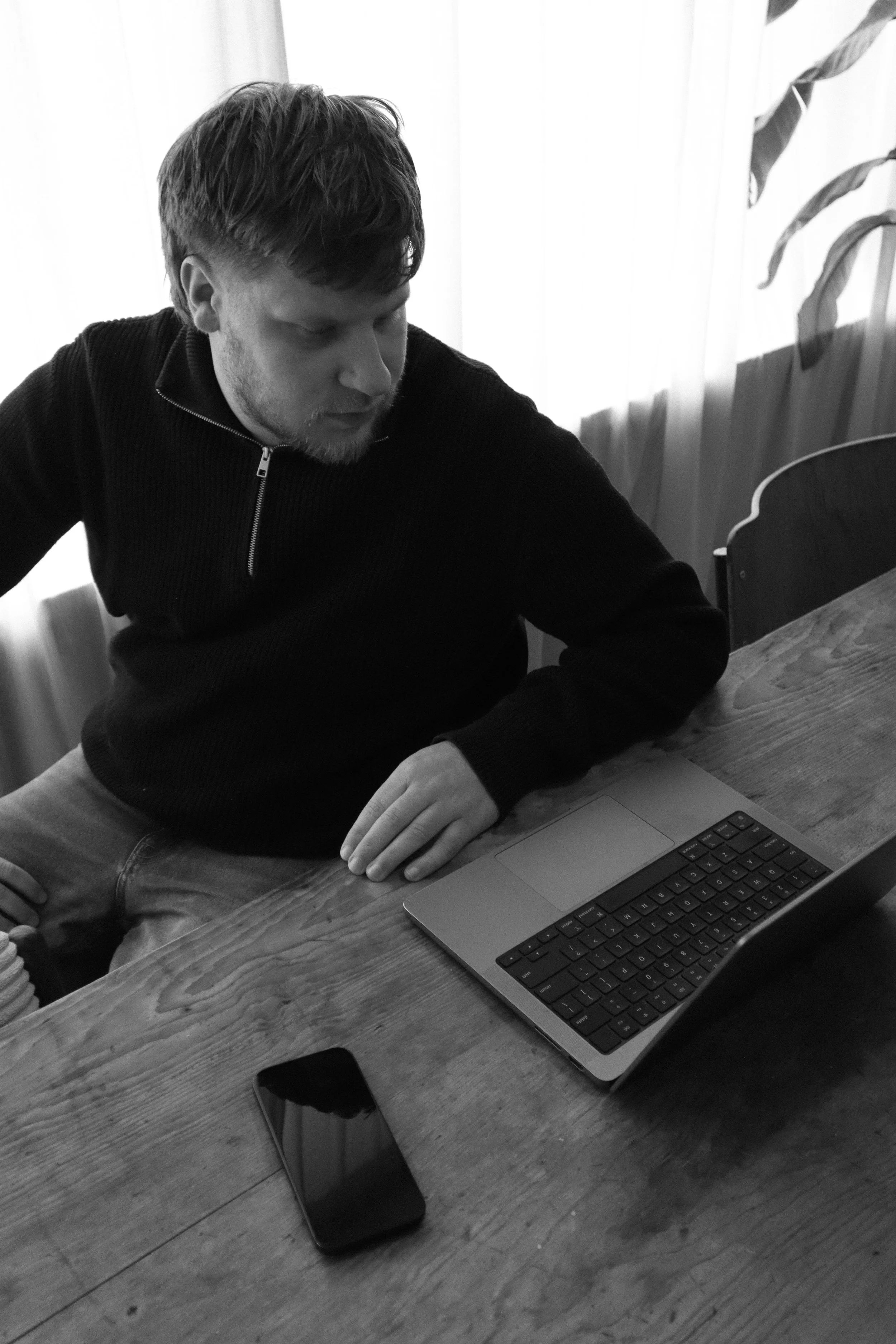 Man zit aan een houten tafel met een laptop en een smartphone.