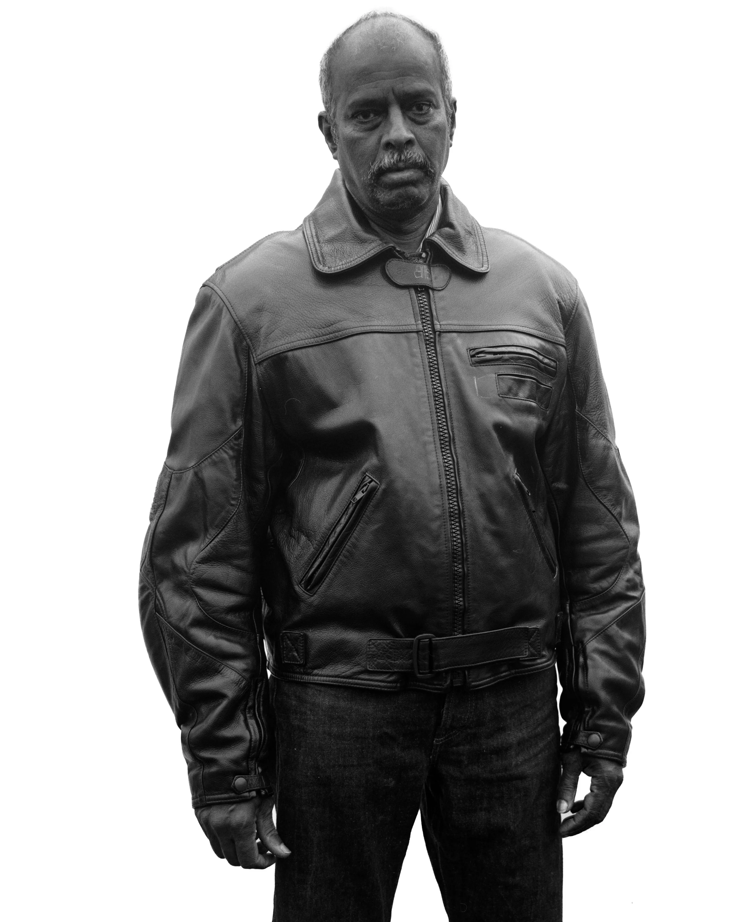 Homme portant une veste en cuir noir, posé contre un fond blanc.