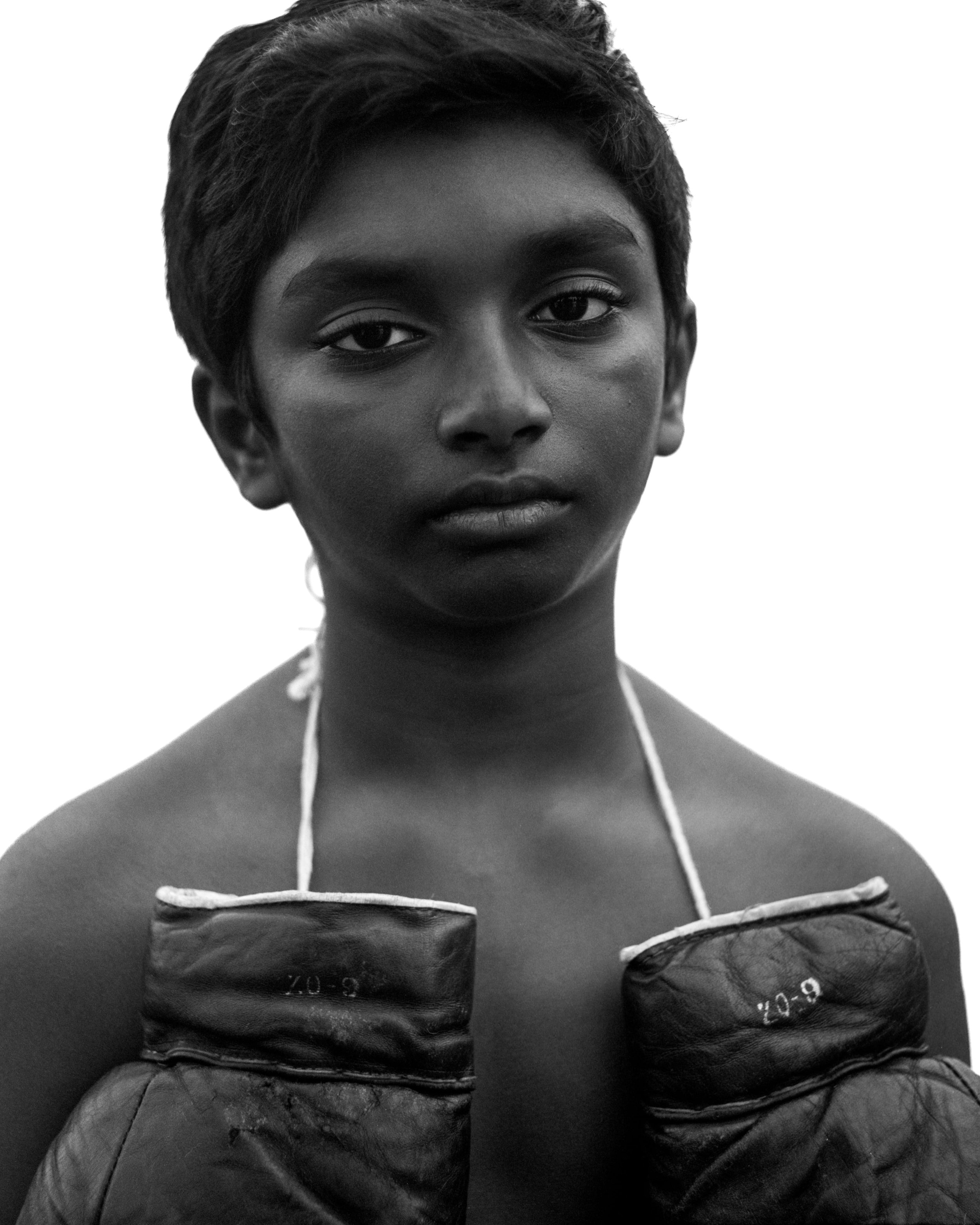 Portrait en noir et blanc d'une jeune femme portant des gants de boxe, regardant sérieusement vers l'avant, avec un fond blanc.