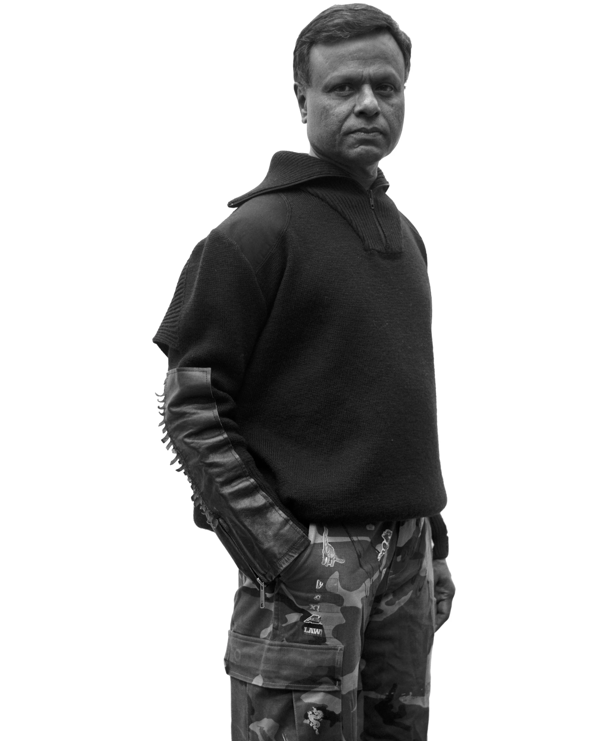 Homme en vêtement noir avec pantalon camouflage, regardant l'appareil, fond blanc.