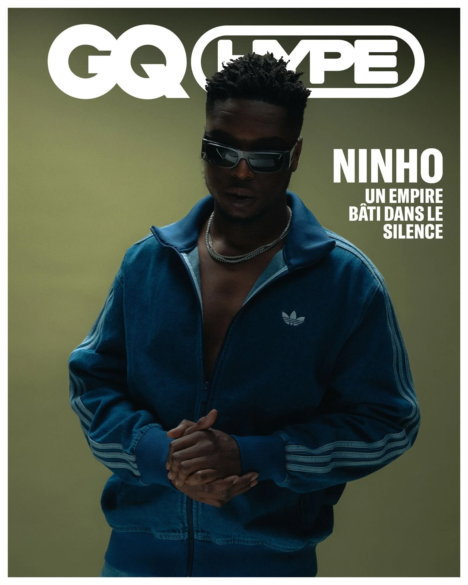 Page de magazine GQ featuring Ninho, portant une veste adidas bleue, lunettes de soleil noires, et une chaîne, avec le texte 'Ninho, un empire bâtit dans le silence'.