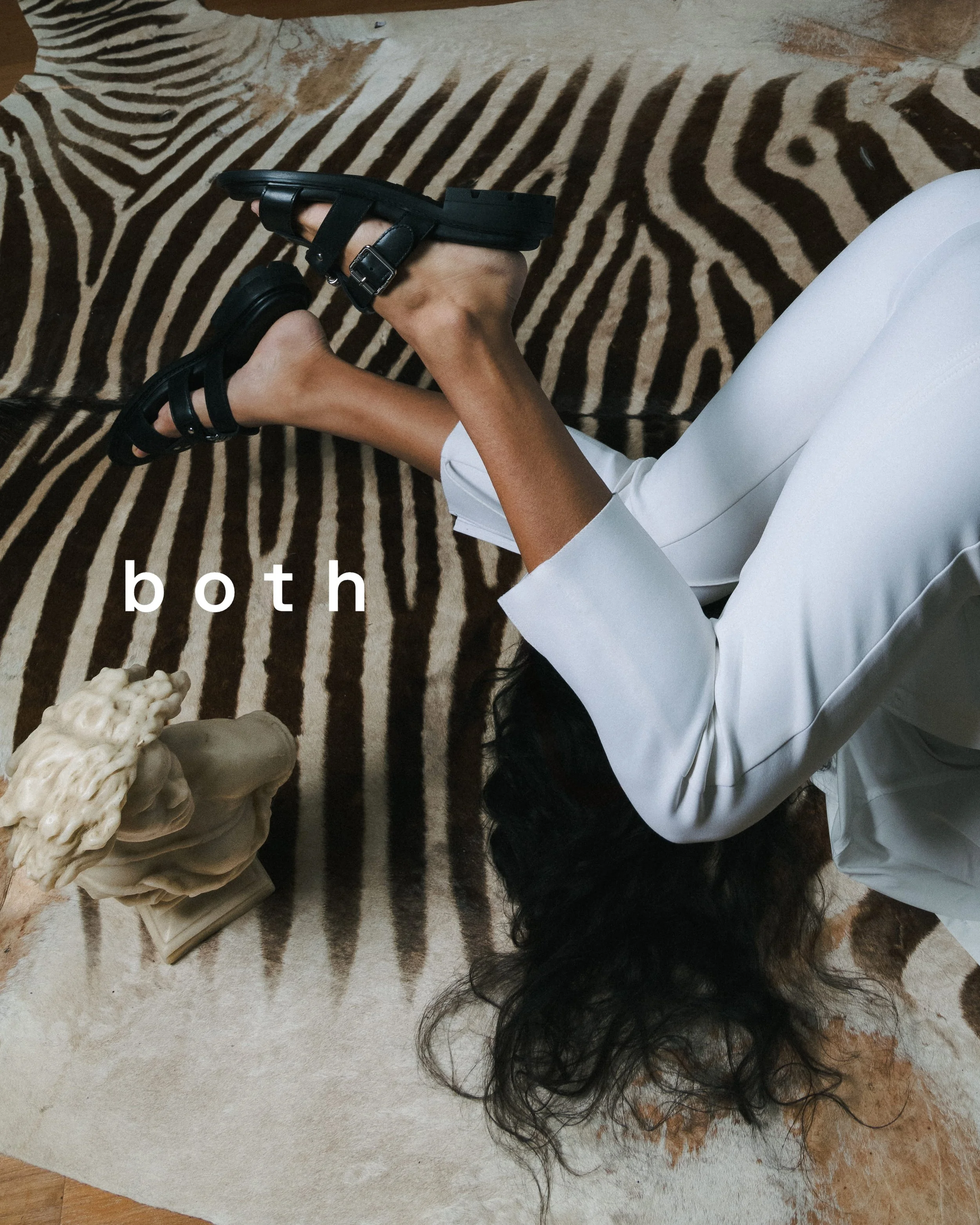 Une personne portant des chaussures noires joue avec un pied dans un tapis zébré. Le mot 'both' est écrit en blanc sur l'image.