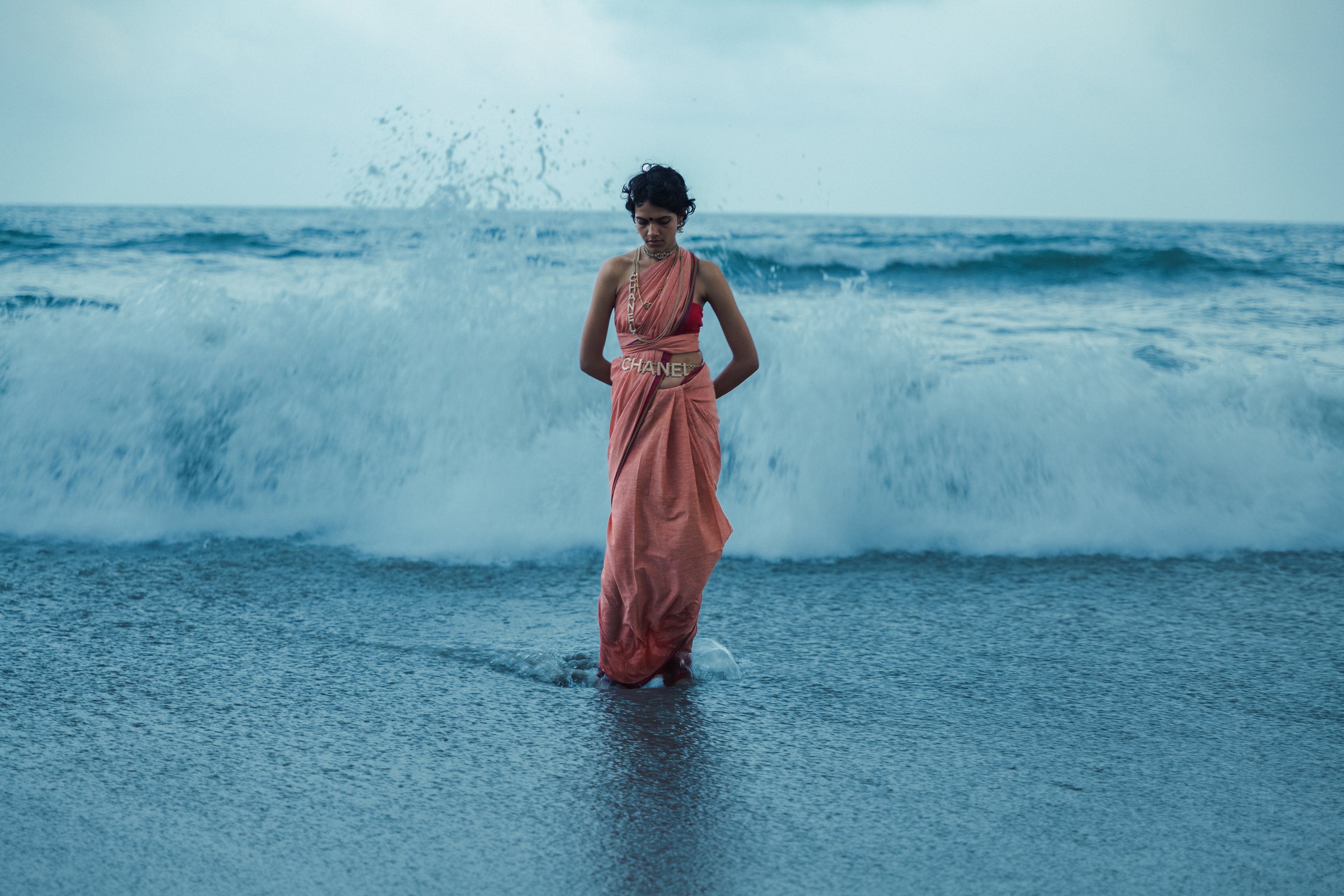 Une femme en robe rose se tient dans l'eau de la mer avec des vagues en arrière-plan