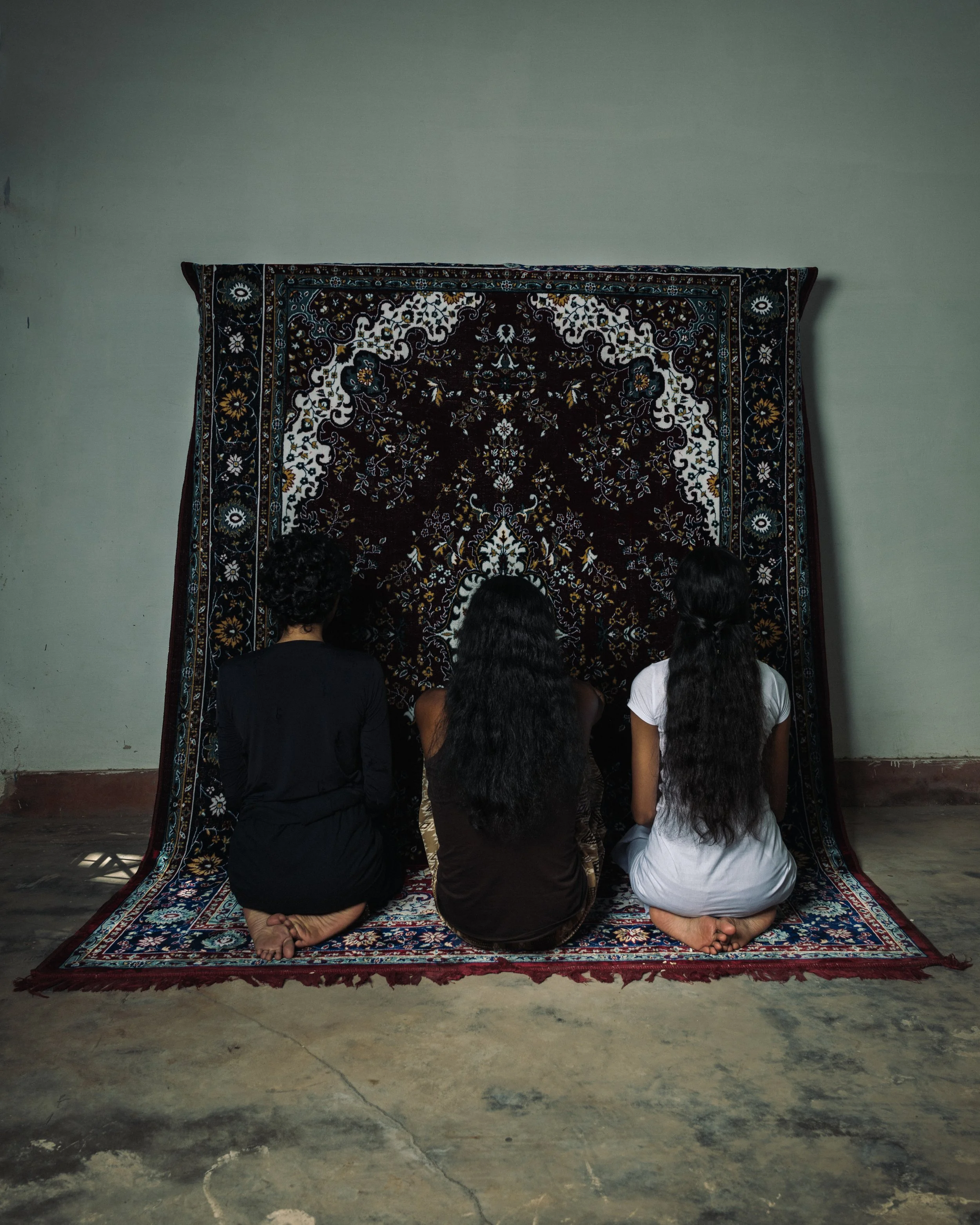Trois femmes assises à genoux devant un tapis orientale suspendu contre un mur