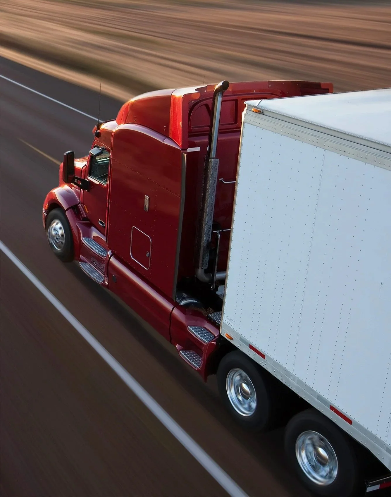 A red semi-truck driving on a highway, viewed from above and to the side.