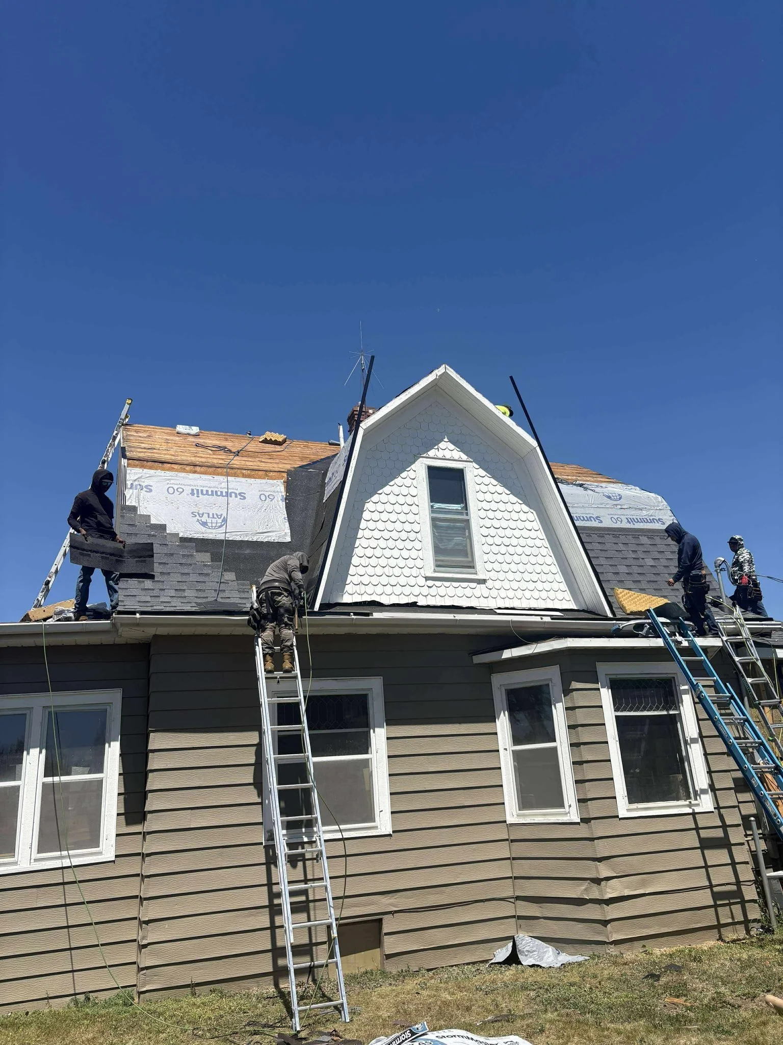 Construction workers installing new roofing shingles on a house under a clear blue sky
