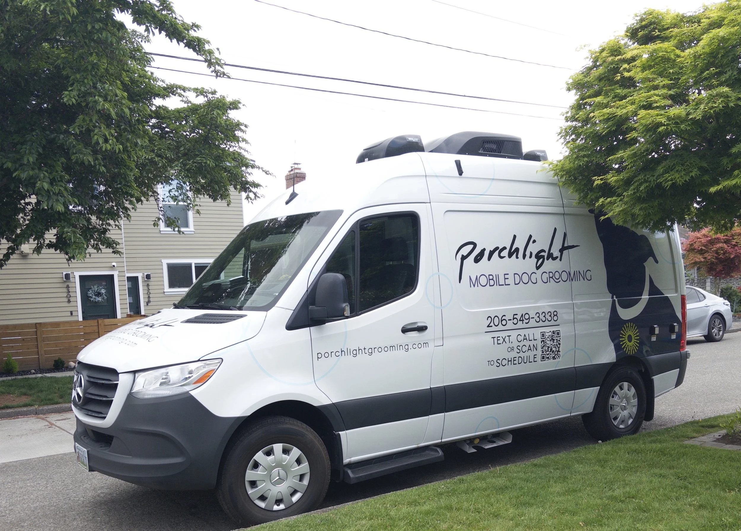 White van with 'Porchlight Mobile Dog Grooming' logo parked on a suburban street, with trees and houses in the background.