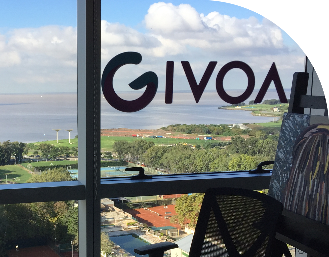 Visão de uma janela com a logo GIVO/ na parte superior. Ao fundo, uma paisagem com um rio, áreas verdes, alguns prédios e uma área de lazer com quadras de tênis. O céu está parcialmente nublado.