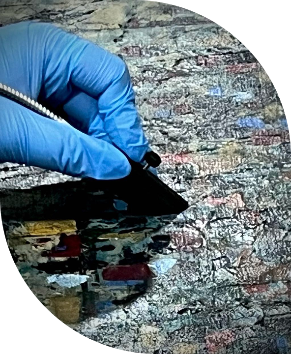 Mão usando luva azul manipulando uma lâmina de corte em um fundo de materiais coloridos.