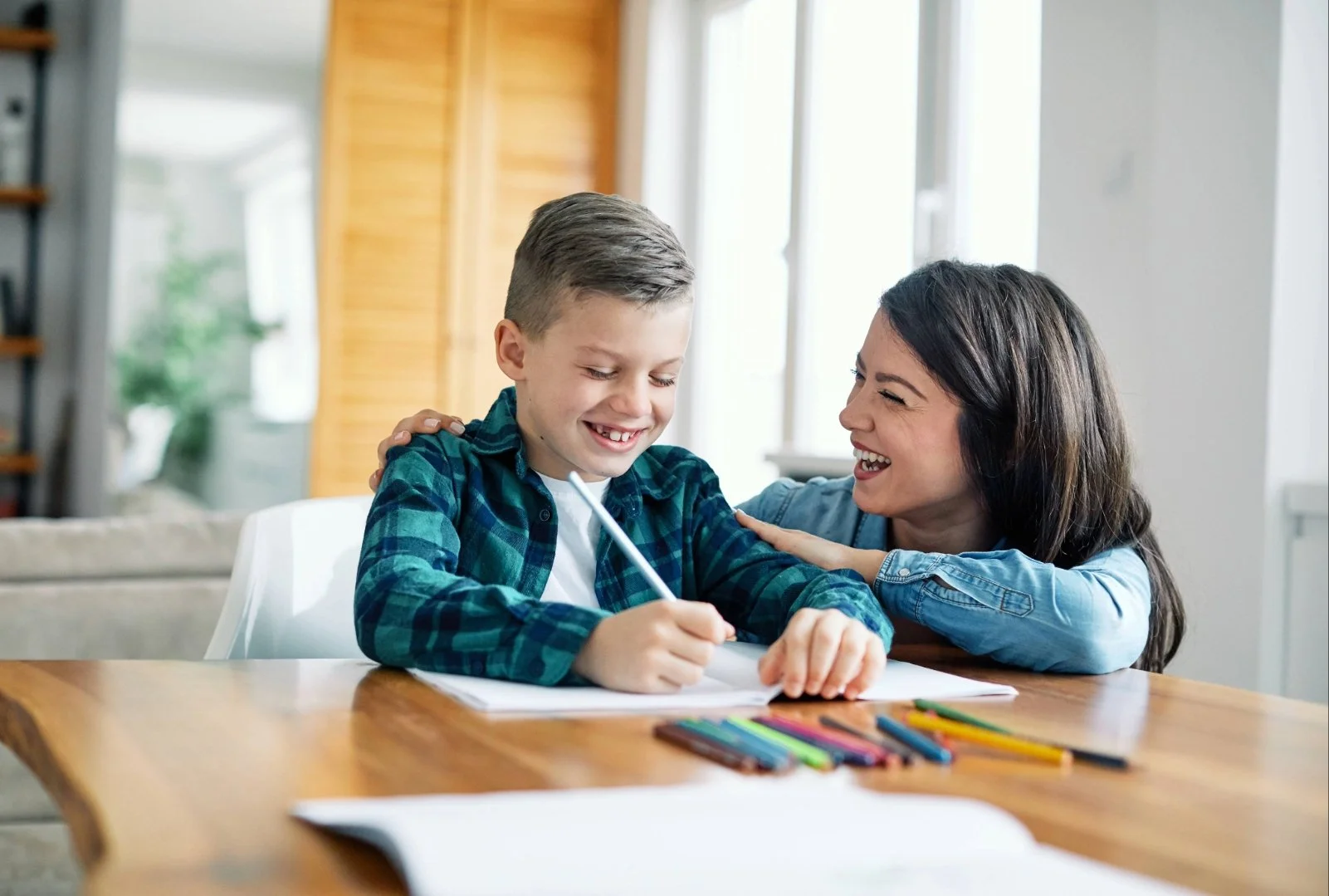 A boy sitting at a wooden table, with a dyslexia therapist, smiling and laughing, during dyslexia therapy in St. Charles, MO.